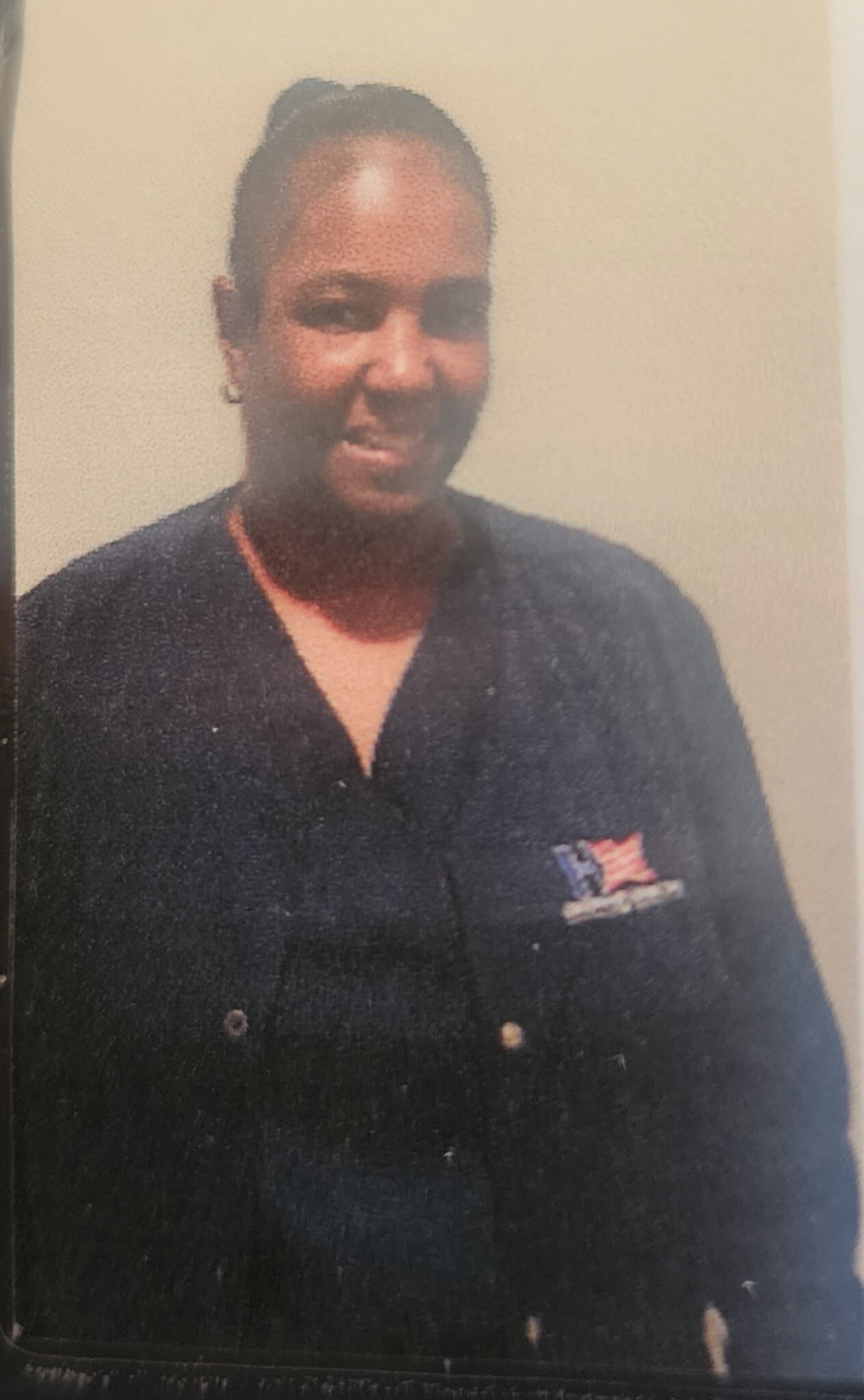 Smiling man in a dark uniform with a small U.S. flag patch on the chest, standing against a neutral background.