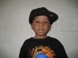 Young child wearing a black shirt with a colorful graphic and a tilted black hat, looking at the camera.