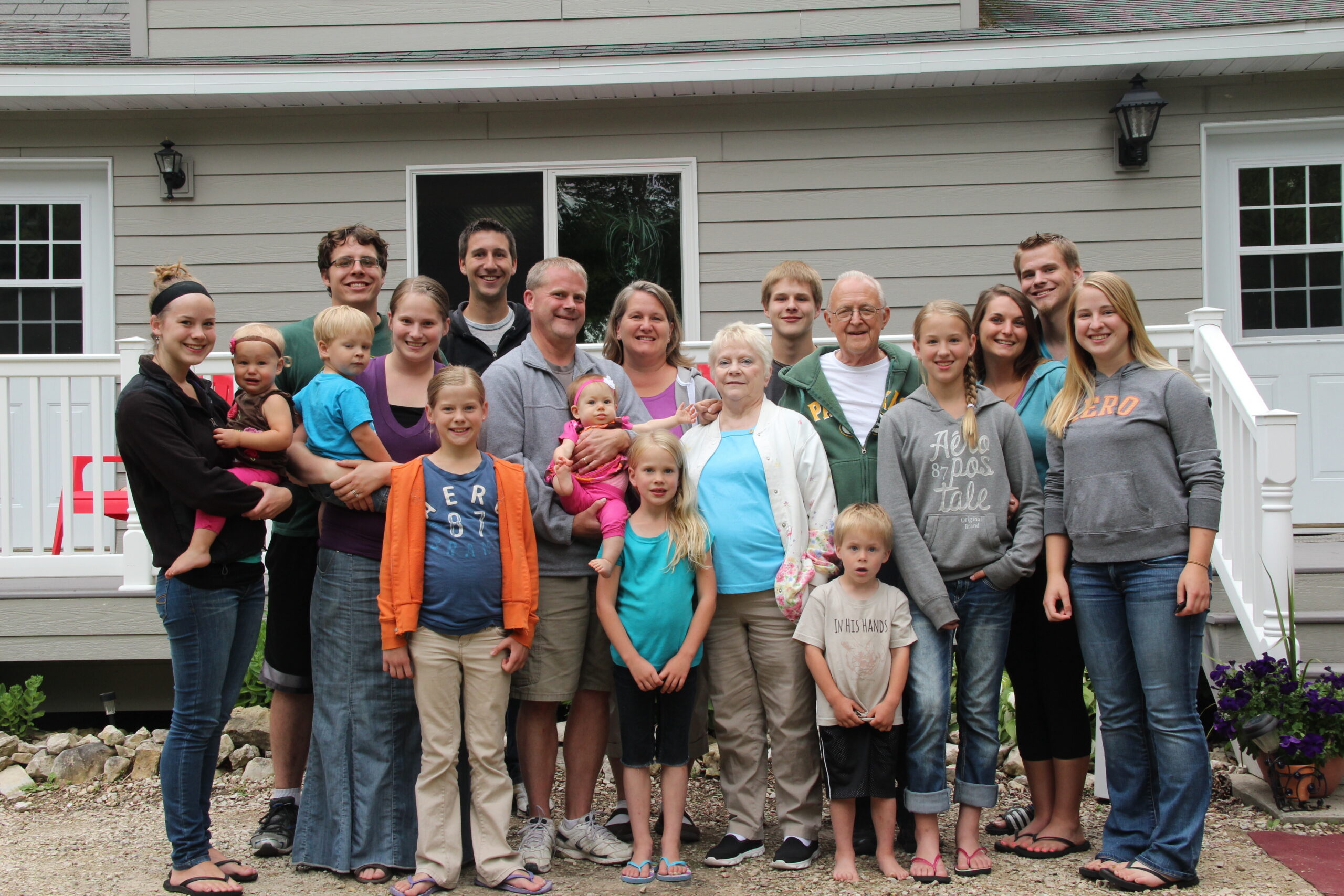 A large group of people of many ages posing together on a front yard and steps of a house.