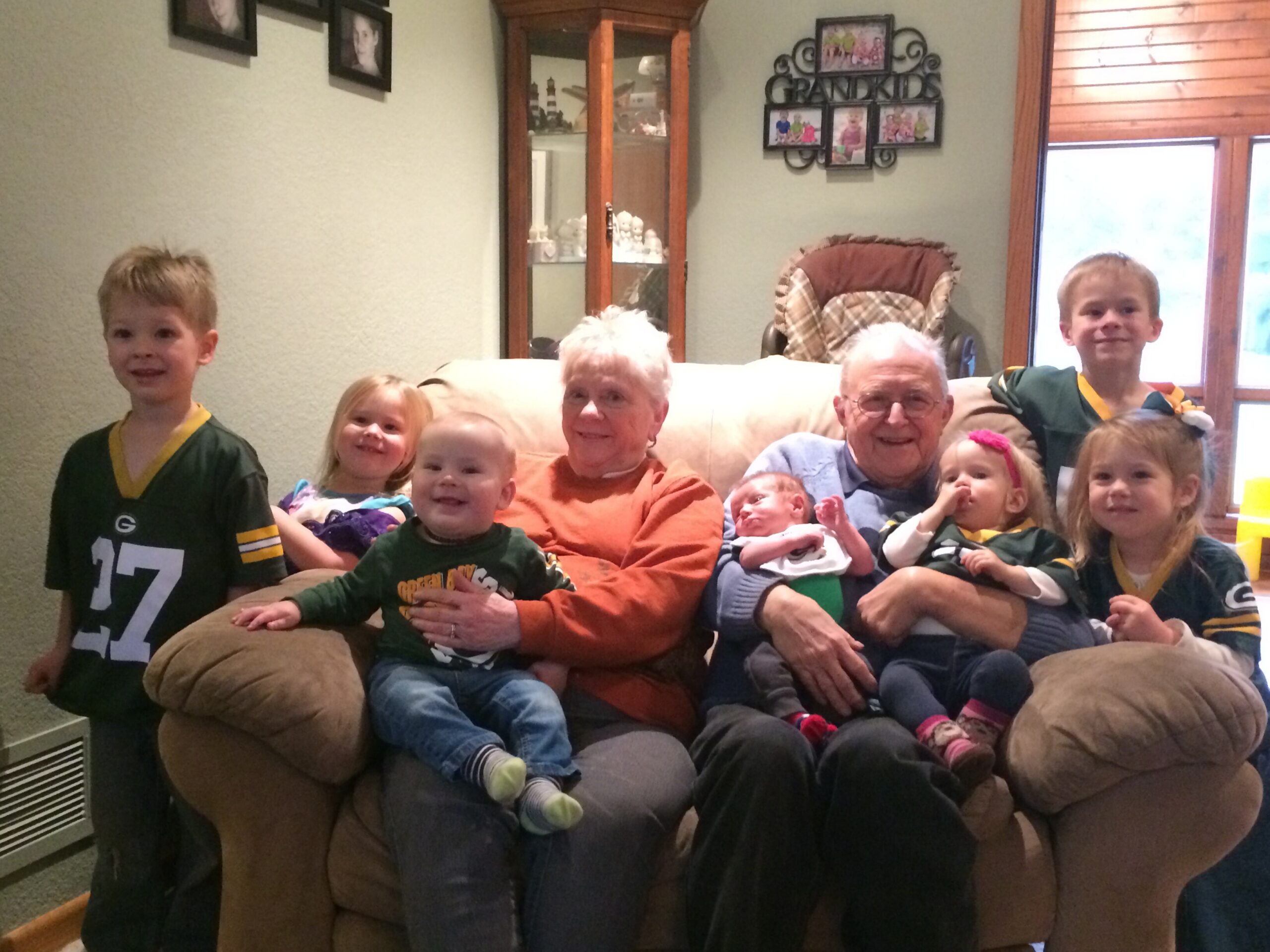 Family group photo on a sofa in a living room, with children and two elderly adults smiling at the camera.