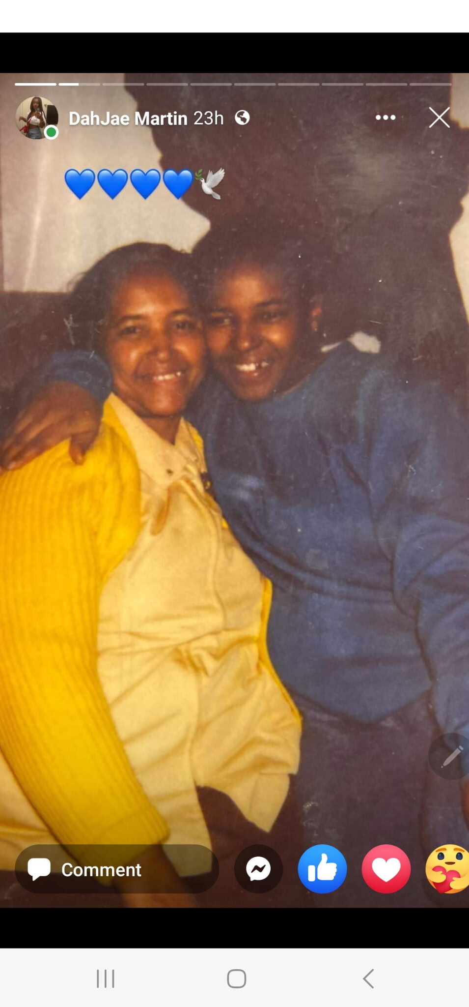 Two women smiling and hugging for a warm photo, one in a yellow cardigan and the other in a blue top/sweater.