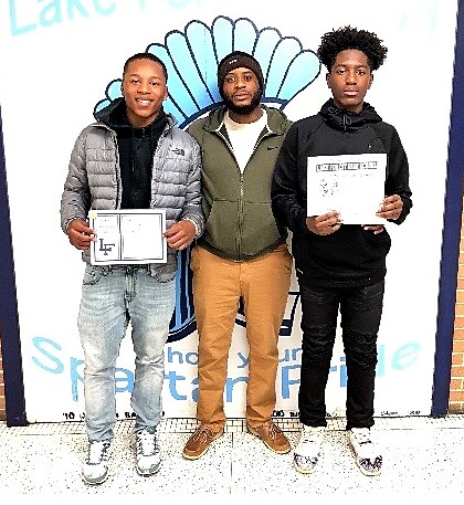 Three young men pose in front of a mural; two hold certificates, celebrating achievement.