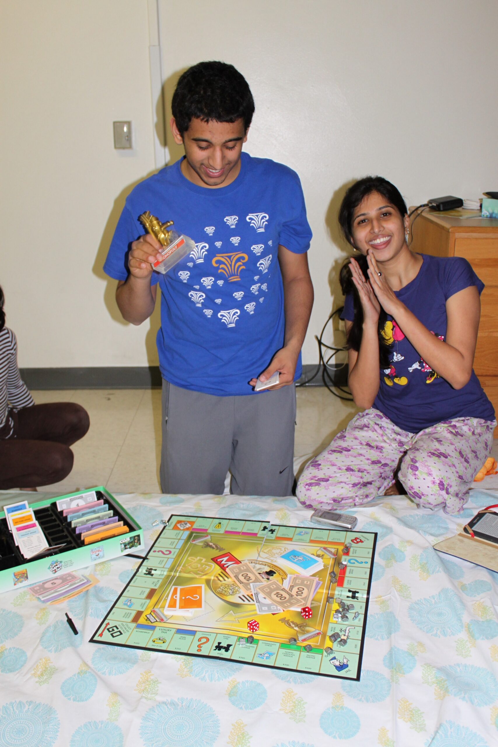Boy in a blue shirt holds a trophy while a smiling girl in purple claps beside a board-game on the table.