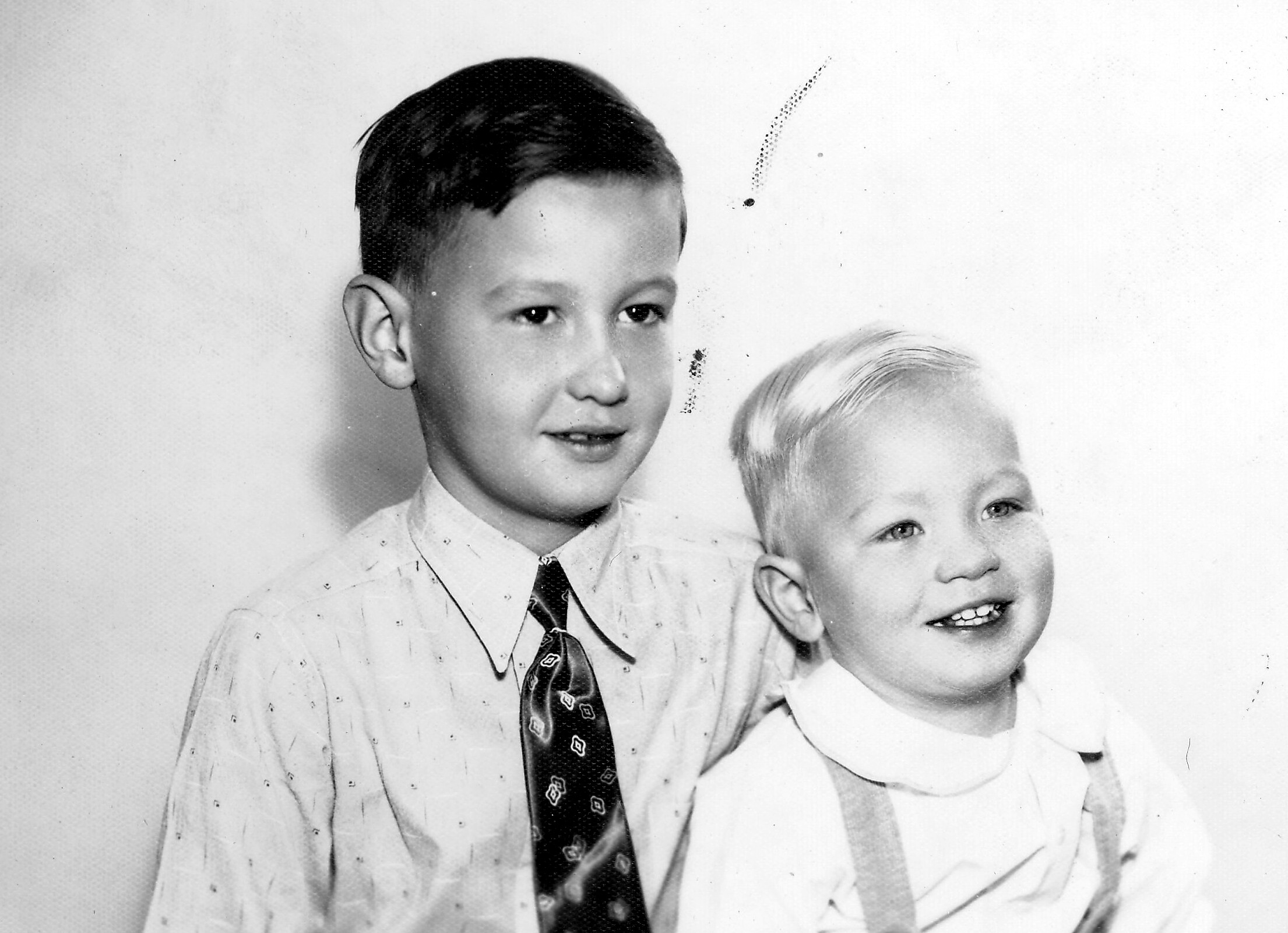 Two young boys in dress shirts posing for a vintage black-and-white portrait, one with a patterned tie and the other smiling slightly to the side.