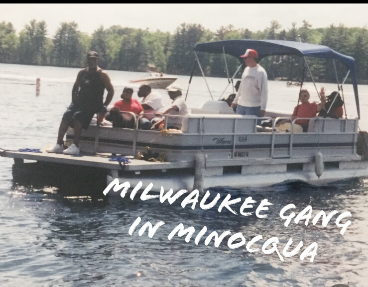 Group of people enjoying a pontoon boat on a lake with trees in the background; overlay text reads 'MILWAUKEE GANG IN MINOCQUA'.