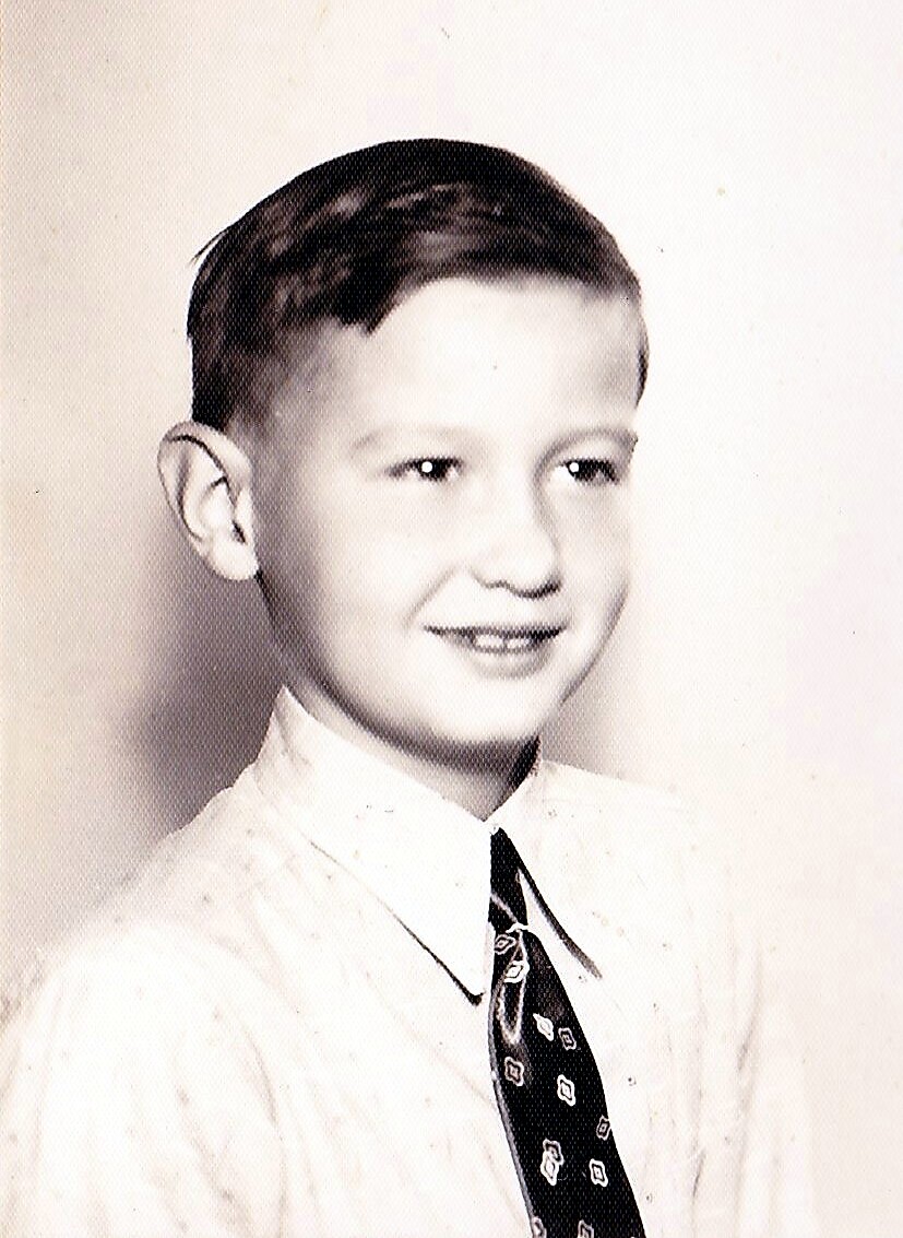 Black-and-white portrait of a smiling boy wearing a dress shirt and patterned tie, looking slightly to the right (school-style portrait).