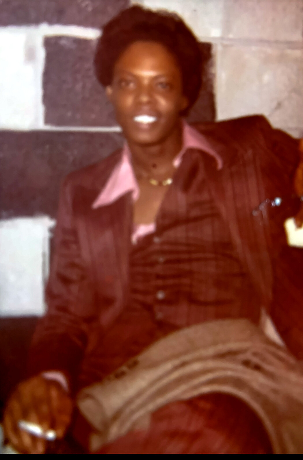 Woman wearing a burgundy blazer and pink blouse, smiling at the camera in an indoor setting.