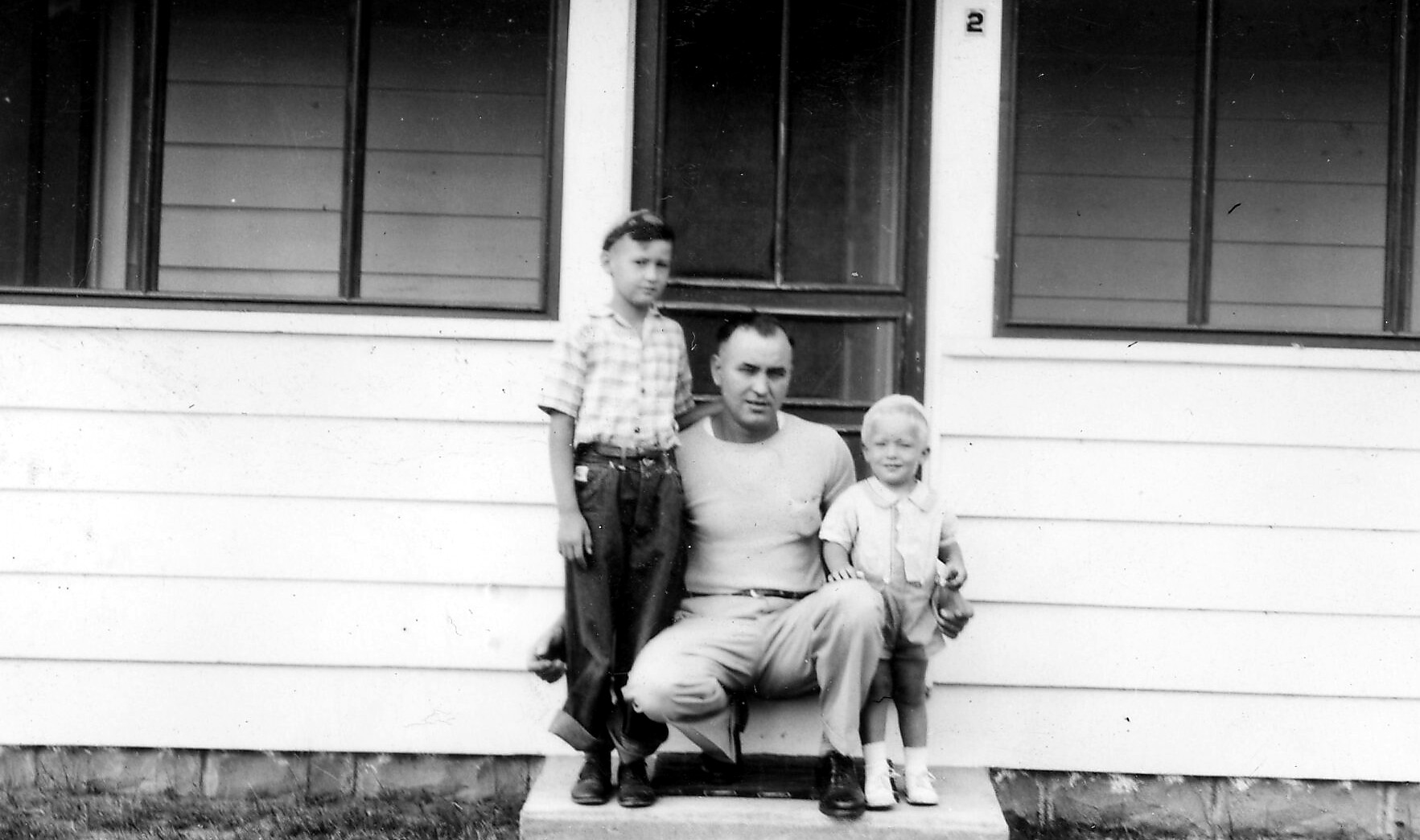 A man kneeling on the front step with two boys, posing for a photo on a house porch.