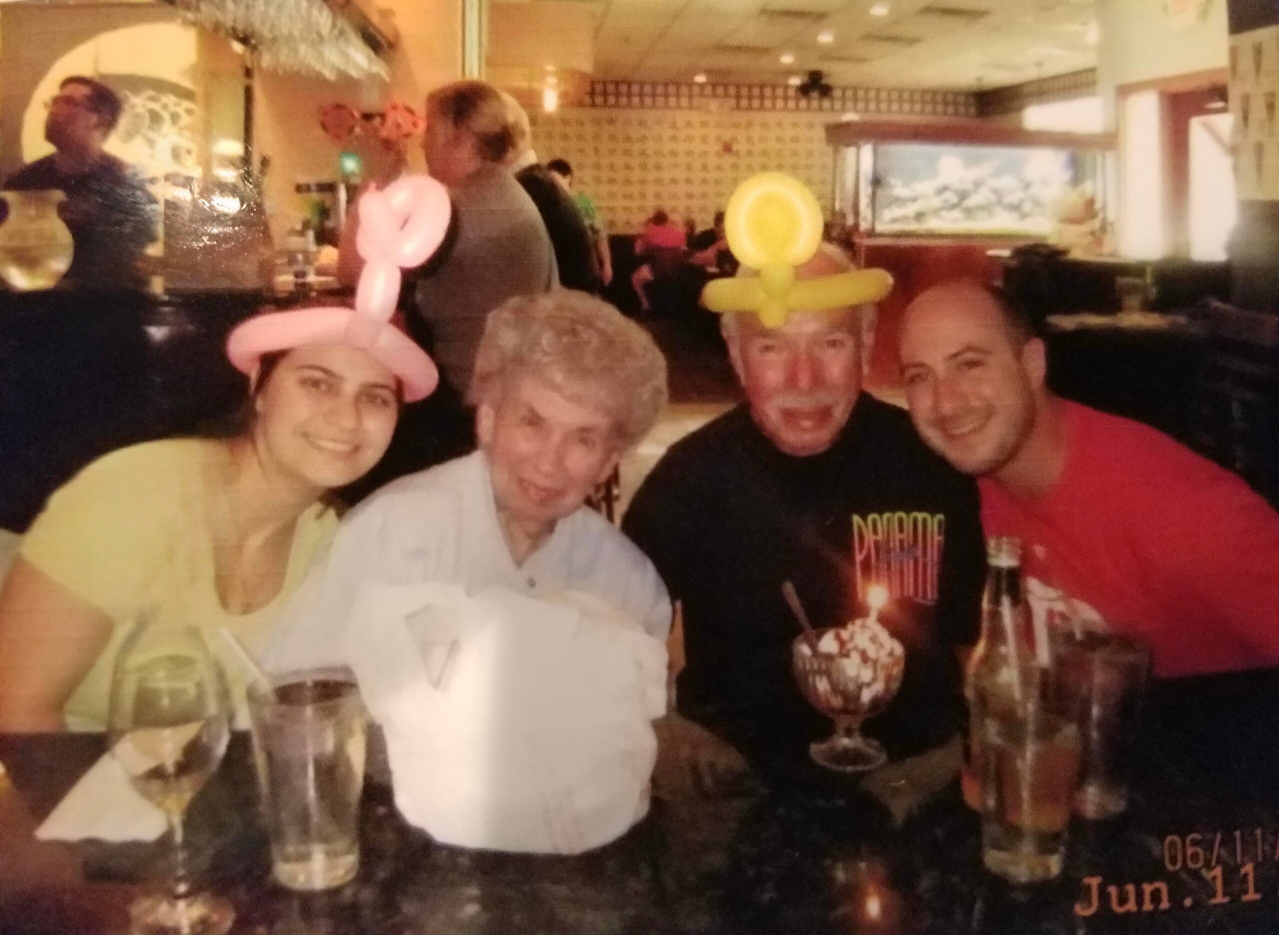 Group of five friends at a restaurant posing for a photo, wearing pink and yellow balloon hats and smiles on their faces.