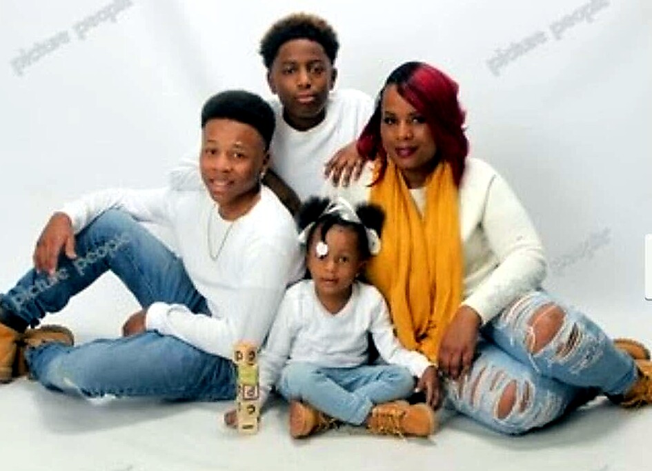 Family portrait: father left in a white shirt and jeans, mother right in a yellow scarf, with two children (little girl in front, teen behind) seated together.