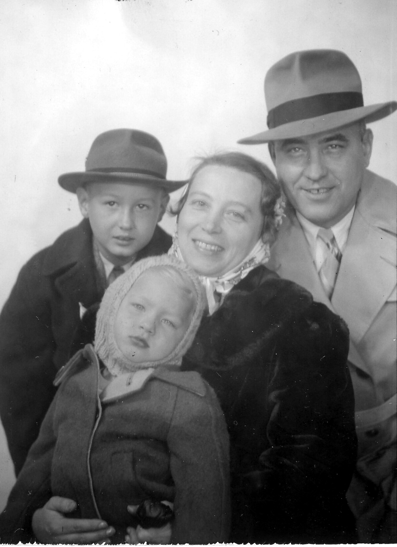 A smiling woman in the center with two children: a boy on the left and a man on the right, all wearing coats and hats in a black-and-white photo.