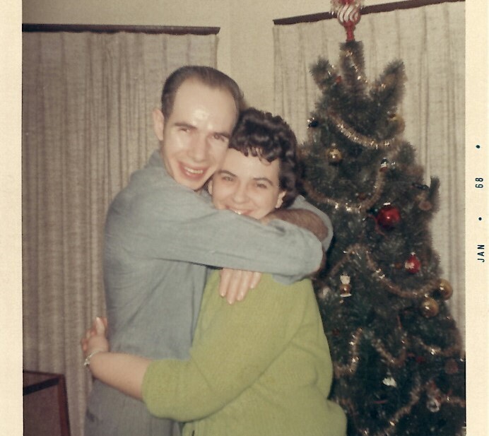 Man and woman embrace in a living room beside a decorated Christmas tree, 1969 photo.