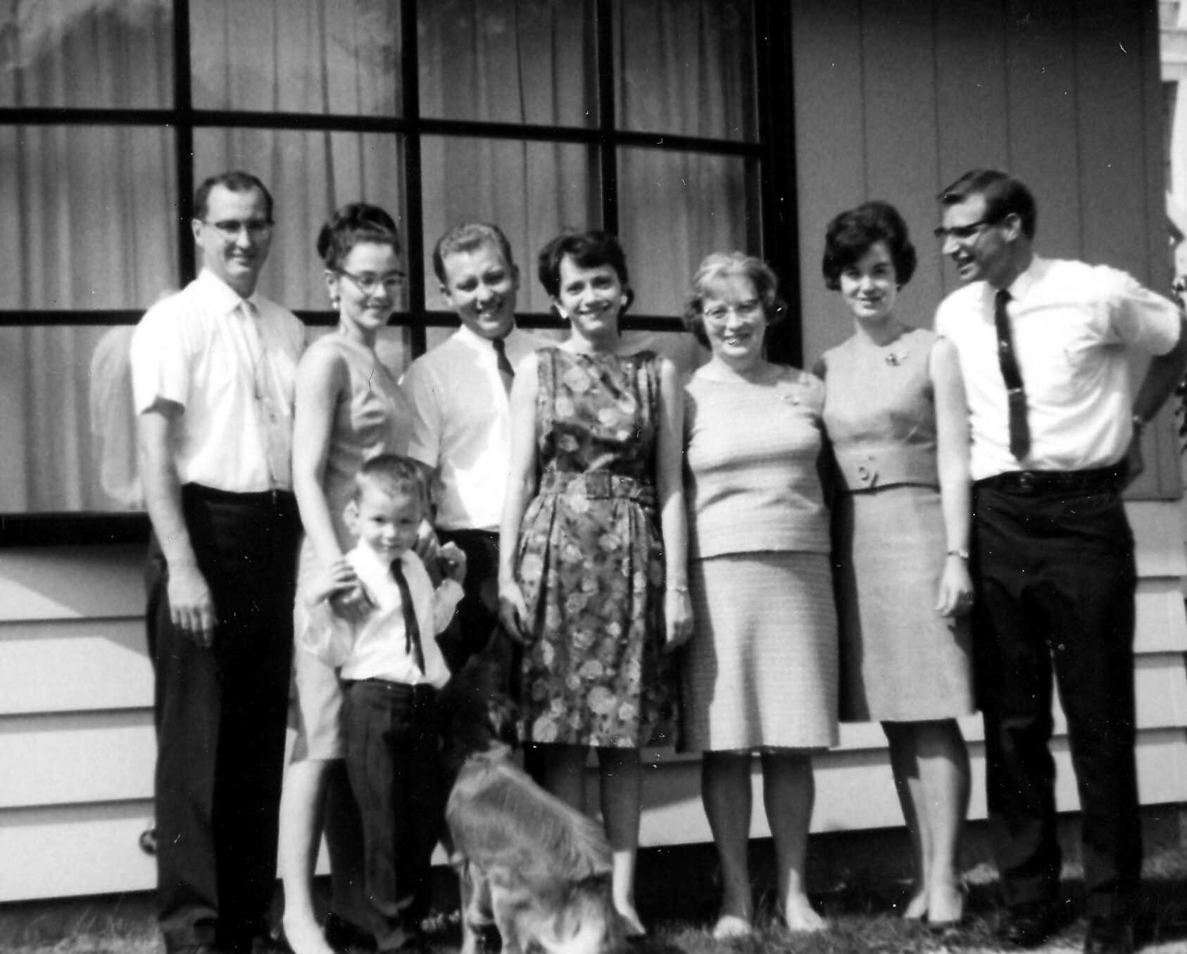 Black-and-white photo of a family posing on front steps of a house, with eight adults and two children smiling at the camera.
