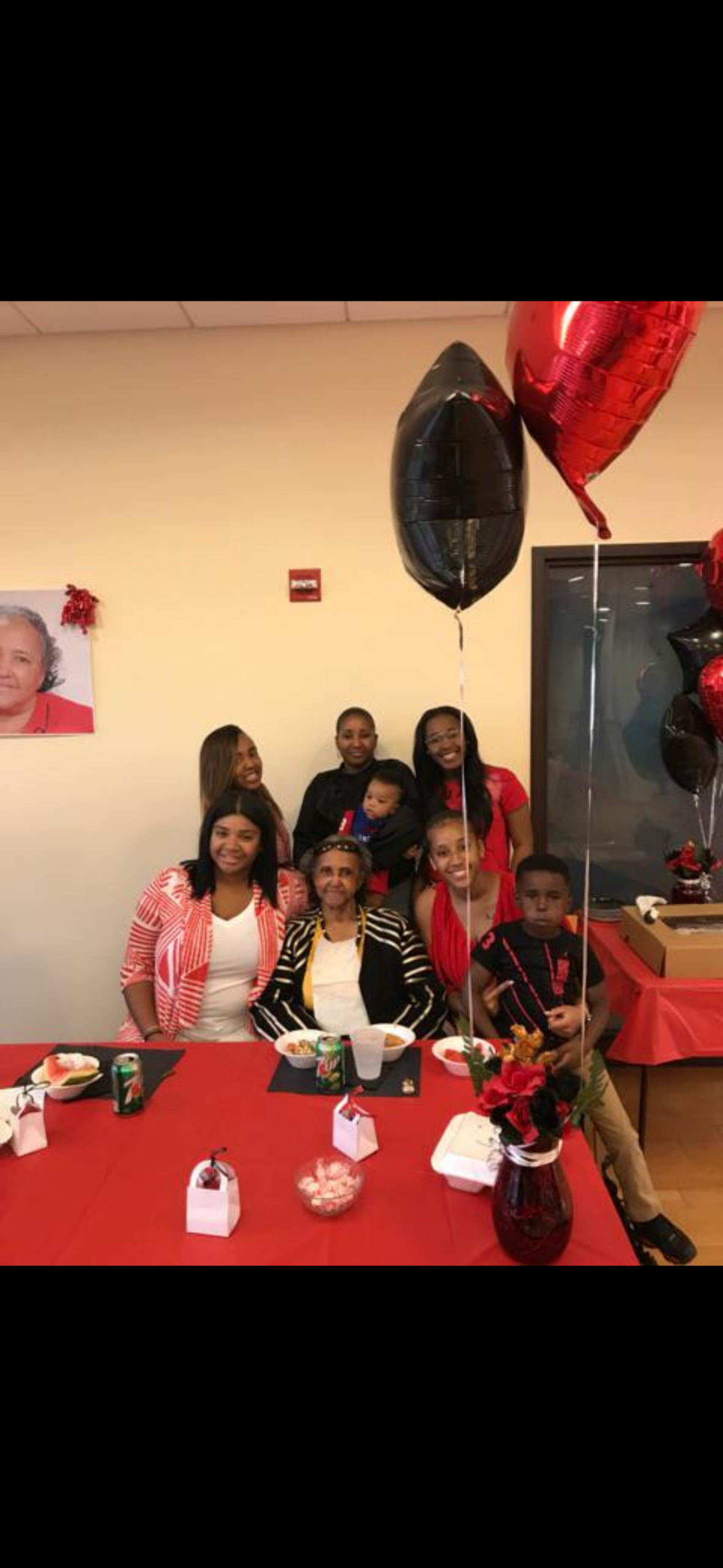 Family group posing for a birthday party around a red-clothed table with balloons and festive decorations in a home setting​ for a celebration.