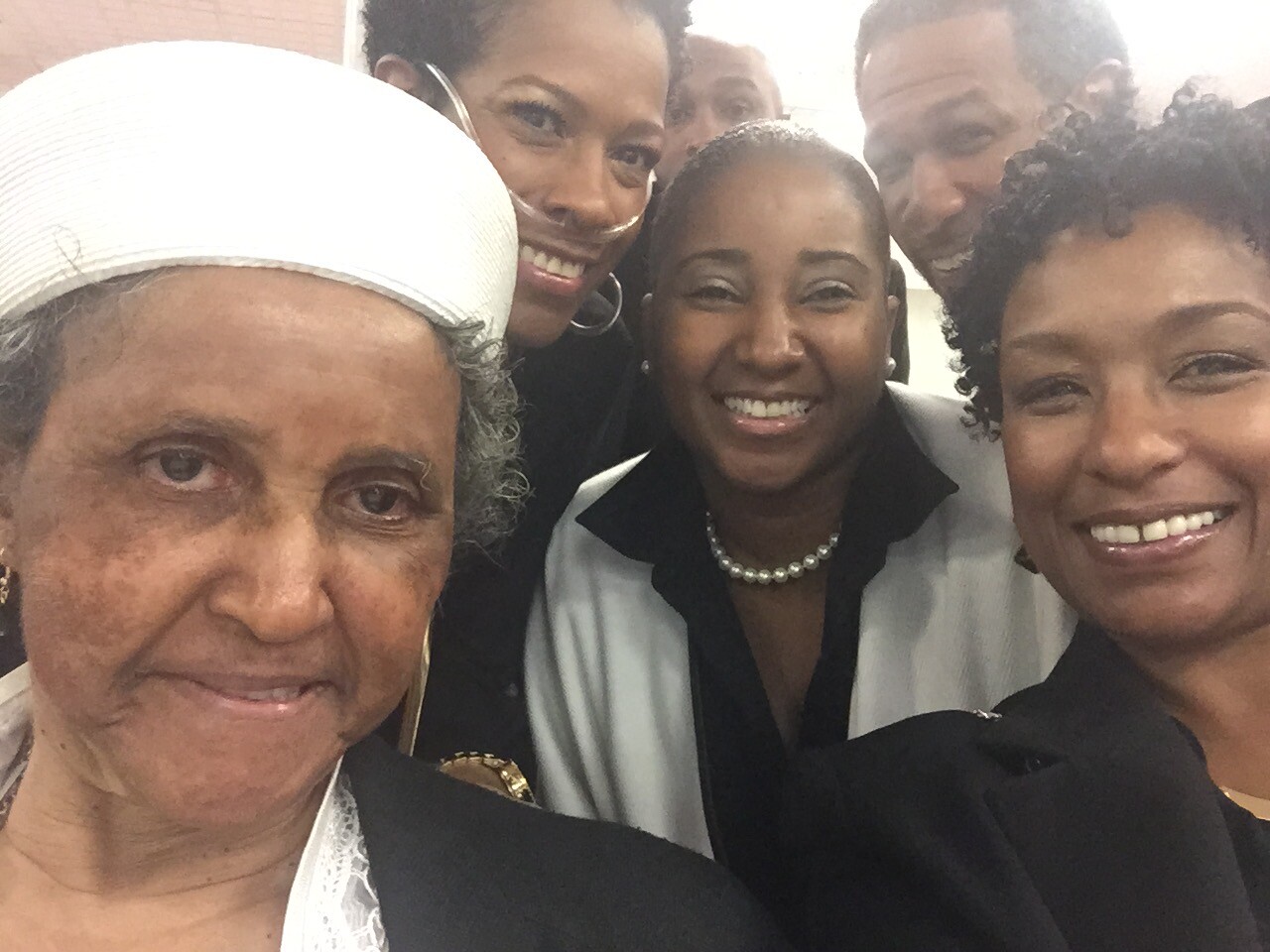 Six people smiling in a close selfie, dressed in business attire.