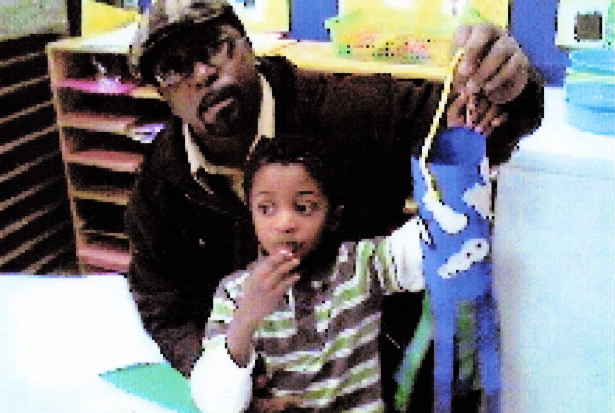 A man holds a young child on his lap in a bright, colorful indoor setting (classroom/child-friendly area).