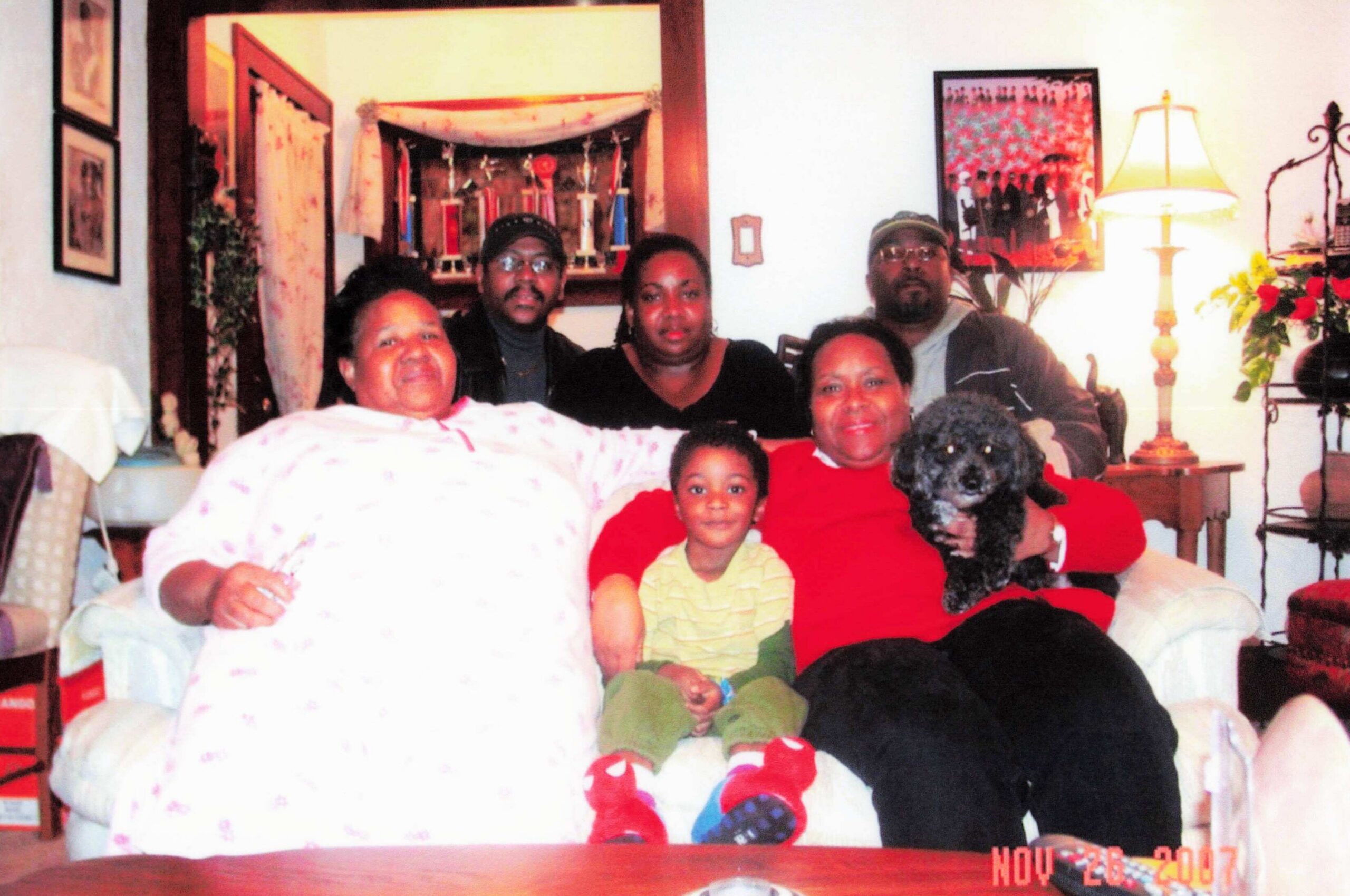 Family group sitting on a sofa in a cozy living room with a black dog in the foreground.