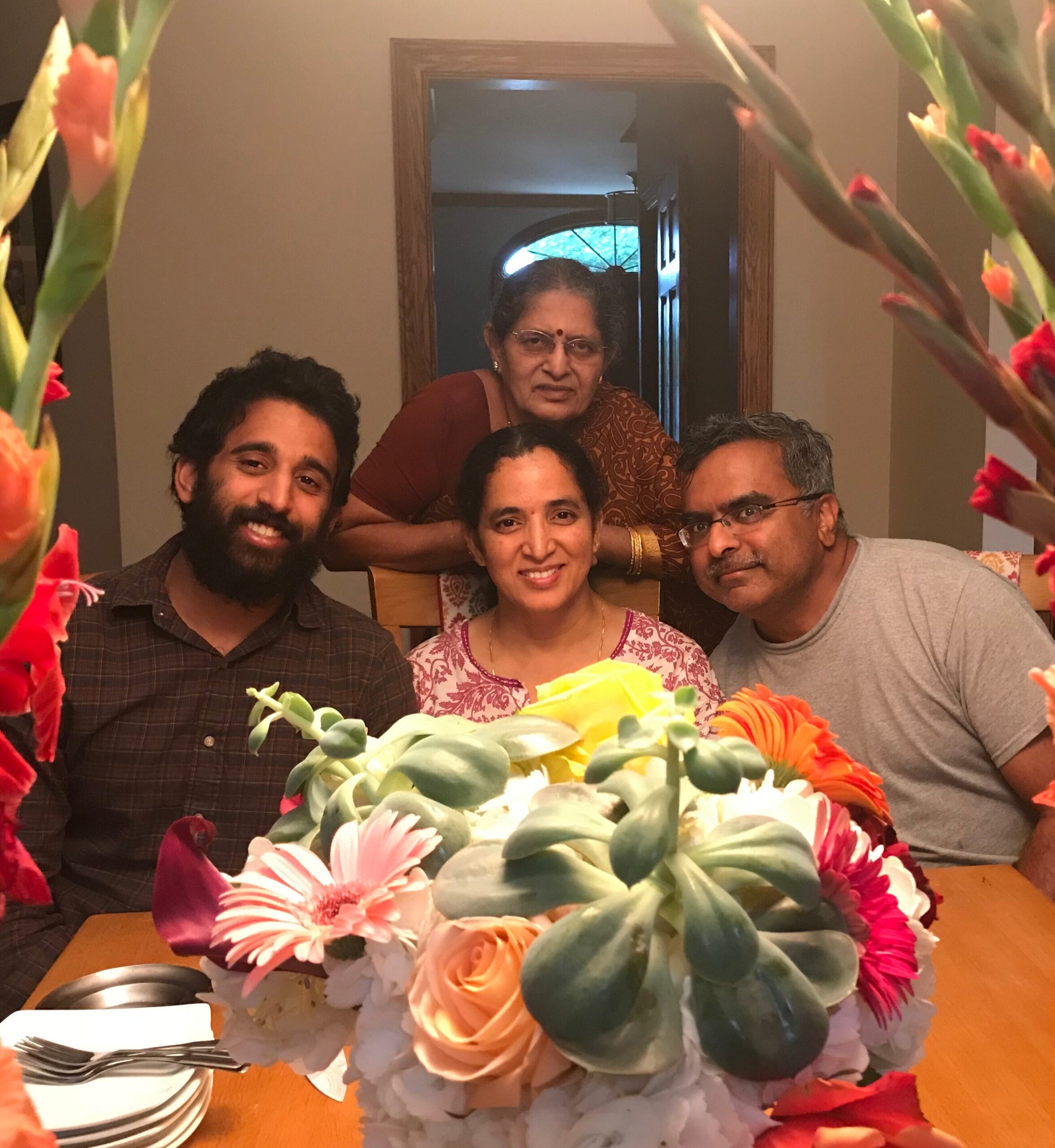 Group photo of five people gathered around a table with a large colorful flower arrangement in front? of them.