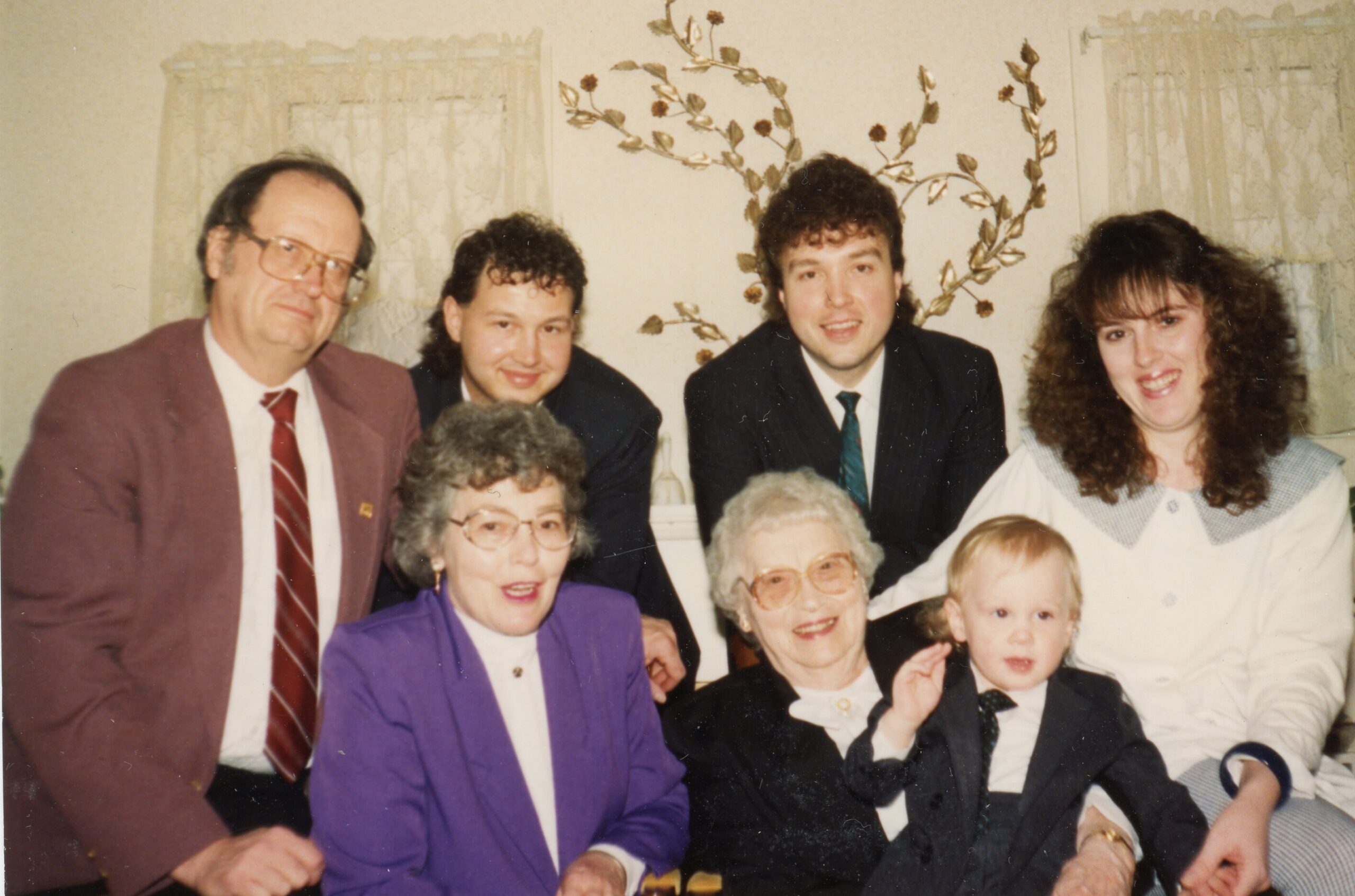 Group of family members posing for a multi-generation photo indoors, smiling at the camera.