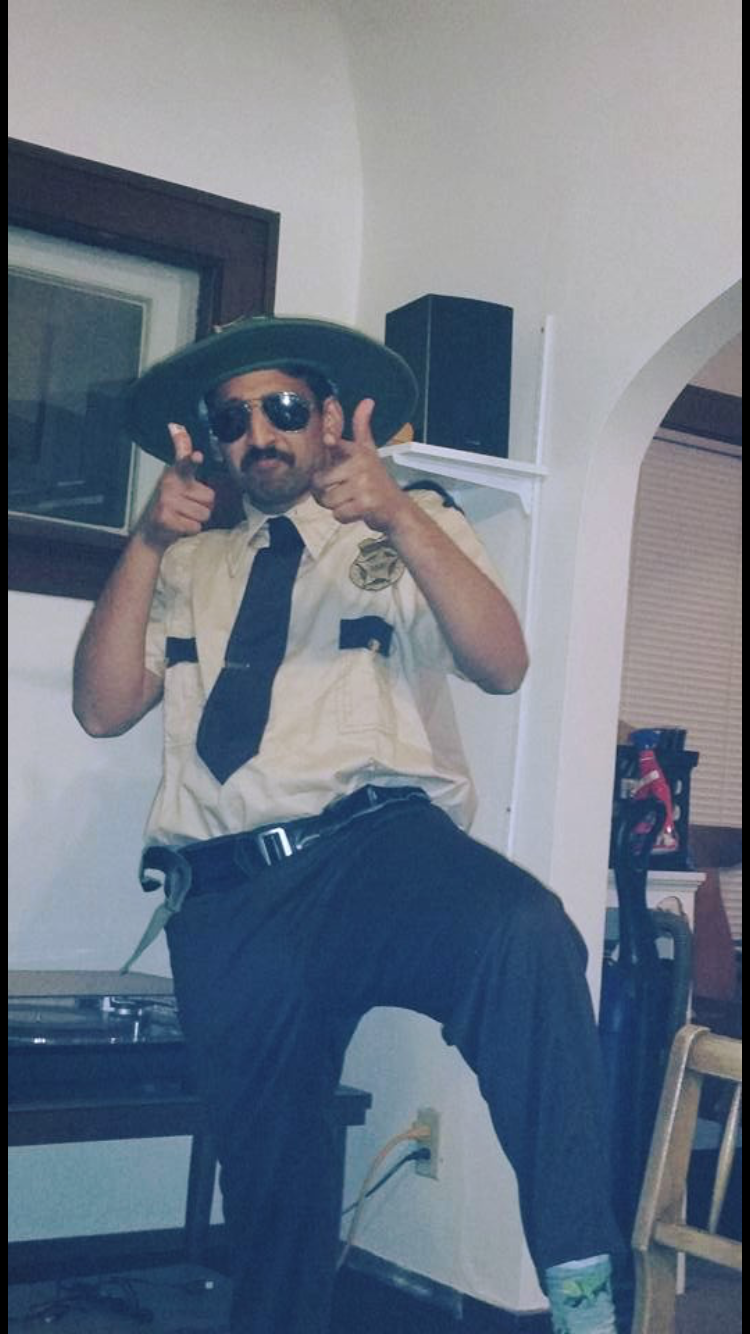 Person in a security uniform with a wide-brim hat and sunglasses, pointing both index fingers at the camera in a playful pose.