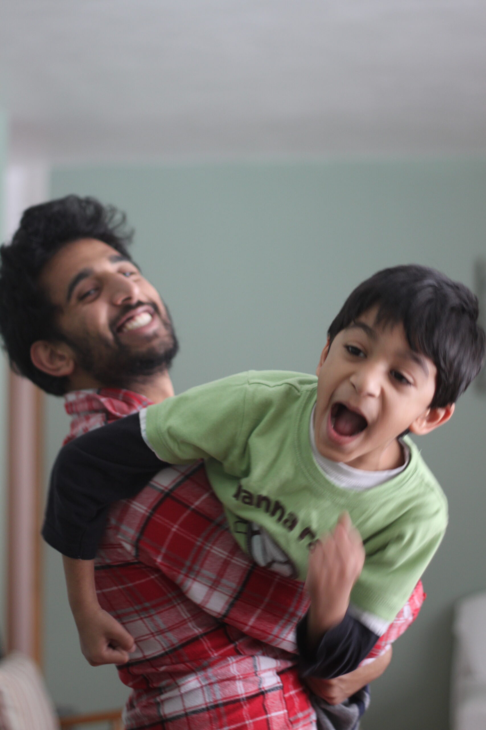 Man carrying a laughing boy on his shoulders indoors during a playful moment.