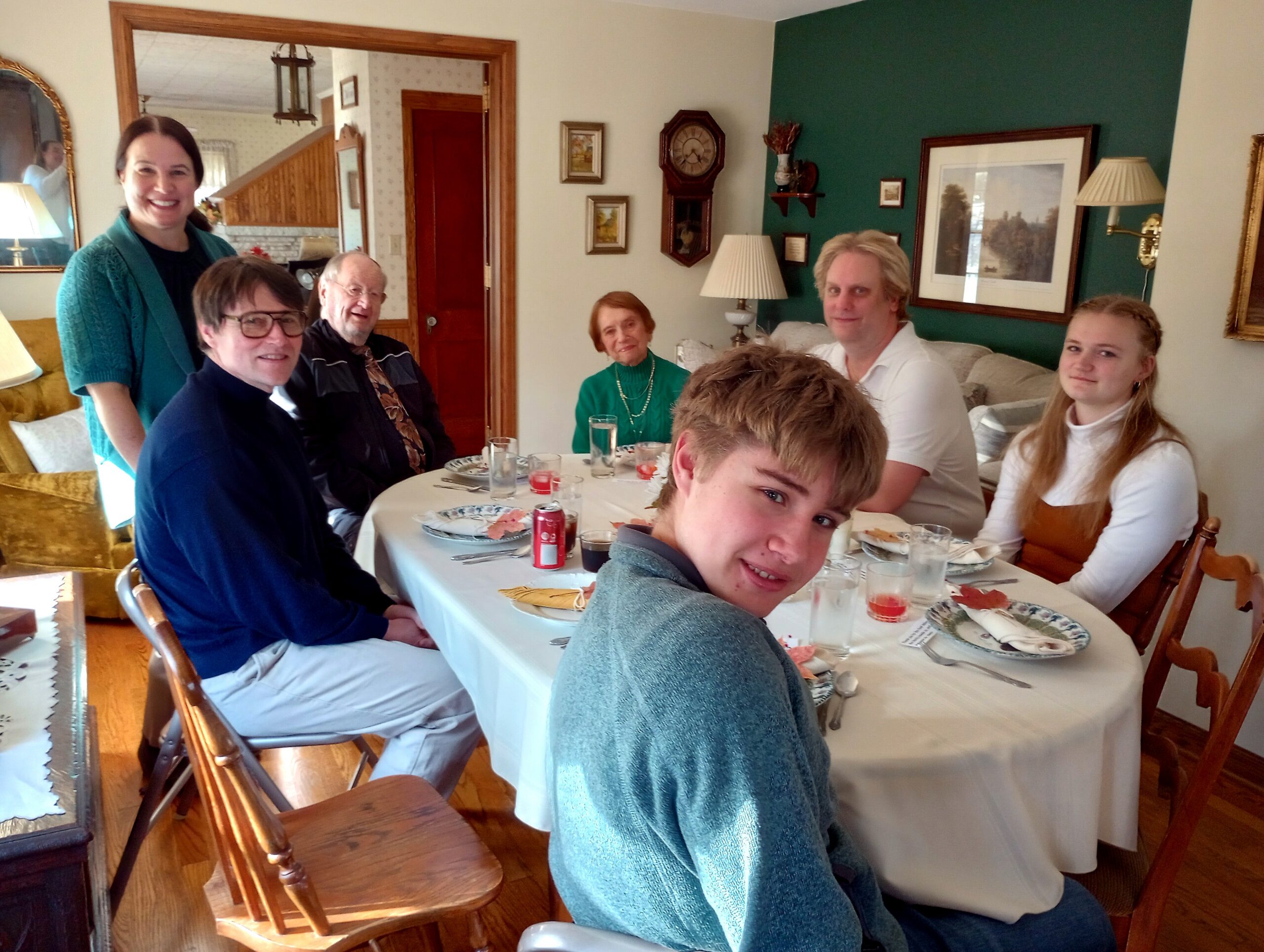 Group of people around a dining table in a cozy living room, smiling and chatting during a meal.