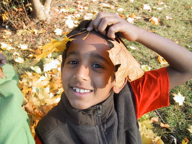 Child outdoors smiling with autumn leaves on his head crown in a park setting