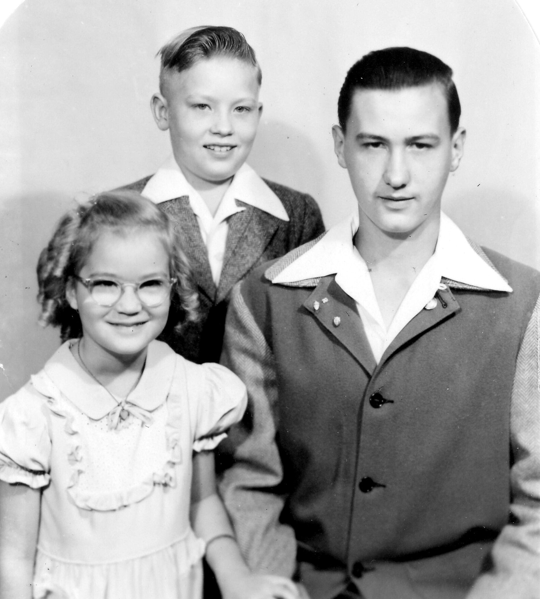 Portrait of three people: a girl with glasses in the foreground left, a smiling boy in a suit behind her, and a man in a dress uniform on the right.