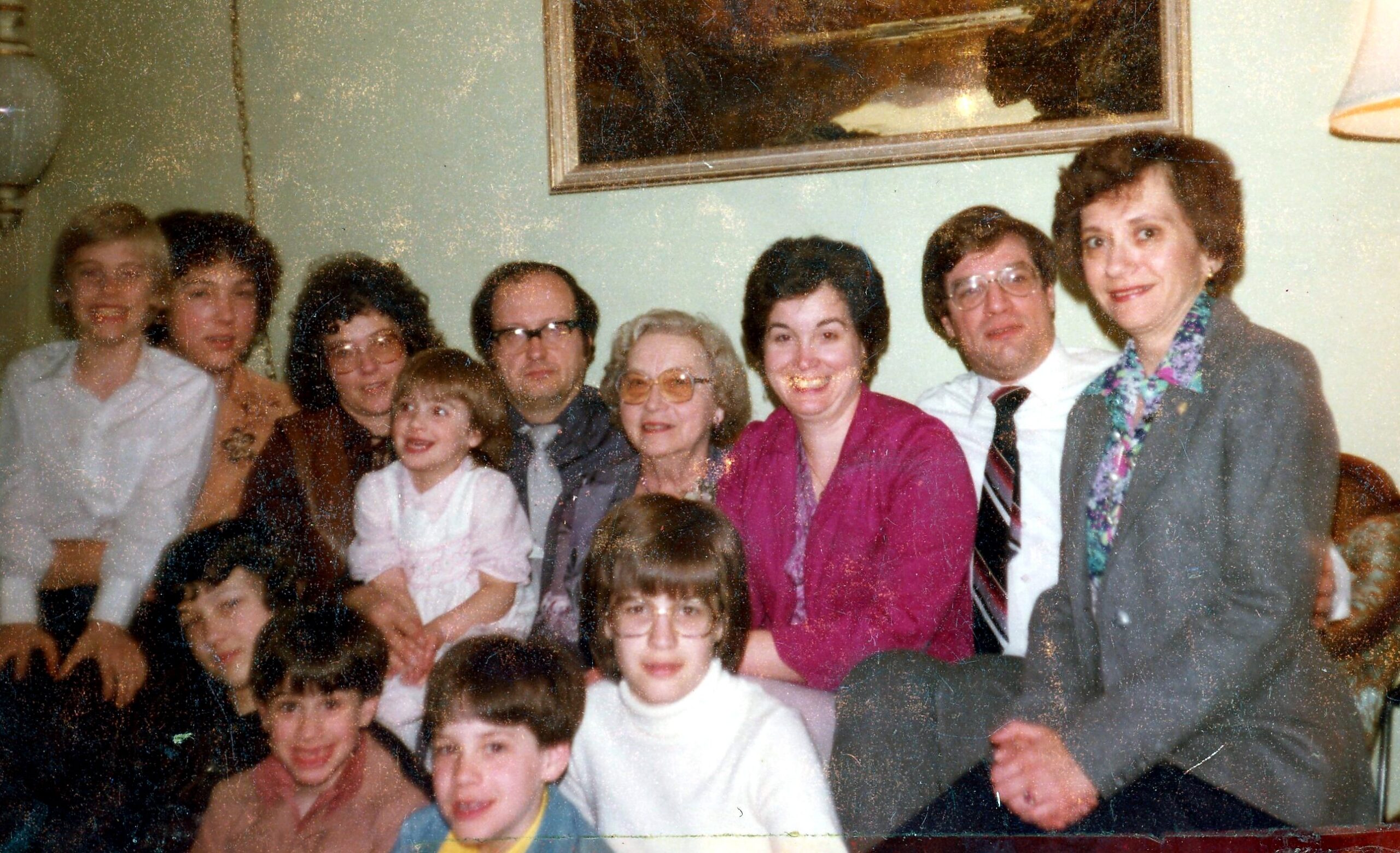 Group of adults and children posing for a family photo in a living room; everyone smiles at the camera (vintage/photo-album style).
