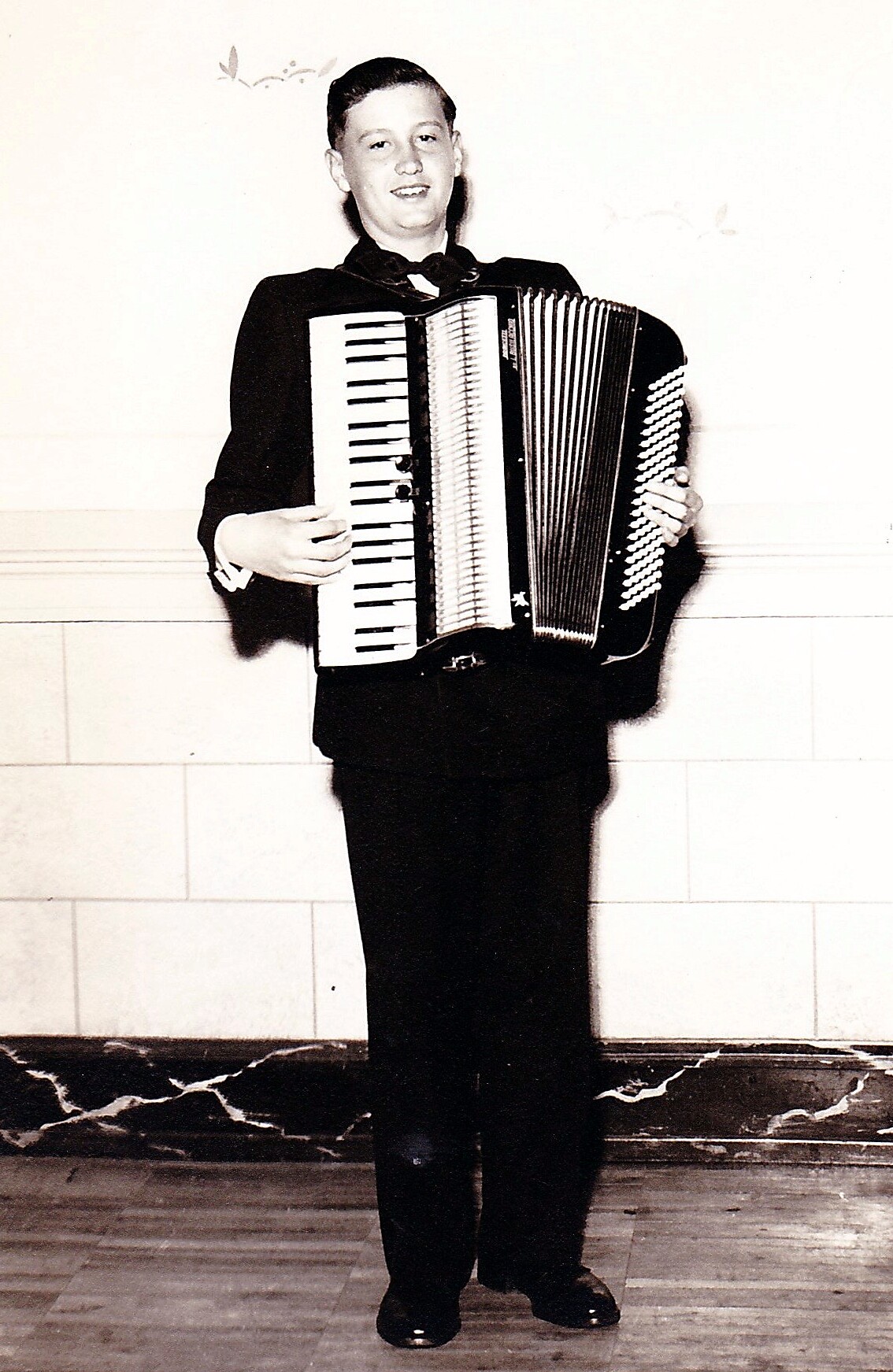 Man in a formal suit playing a large accordion indoors.