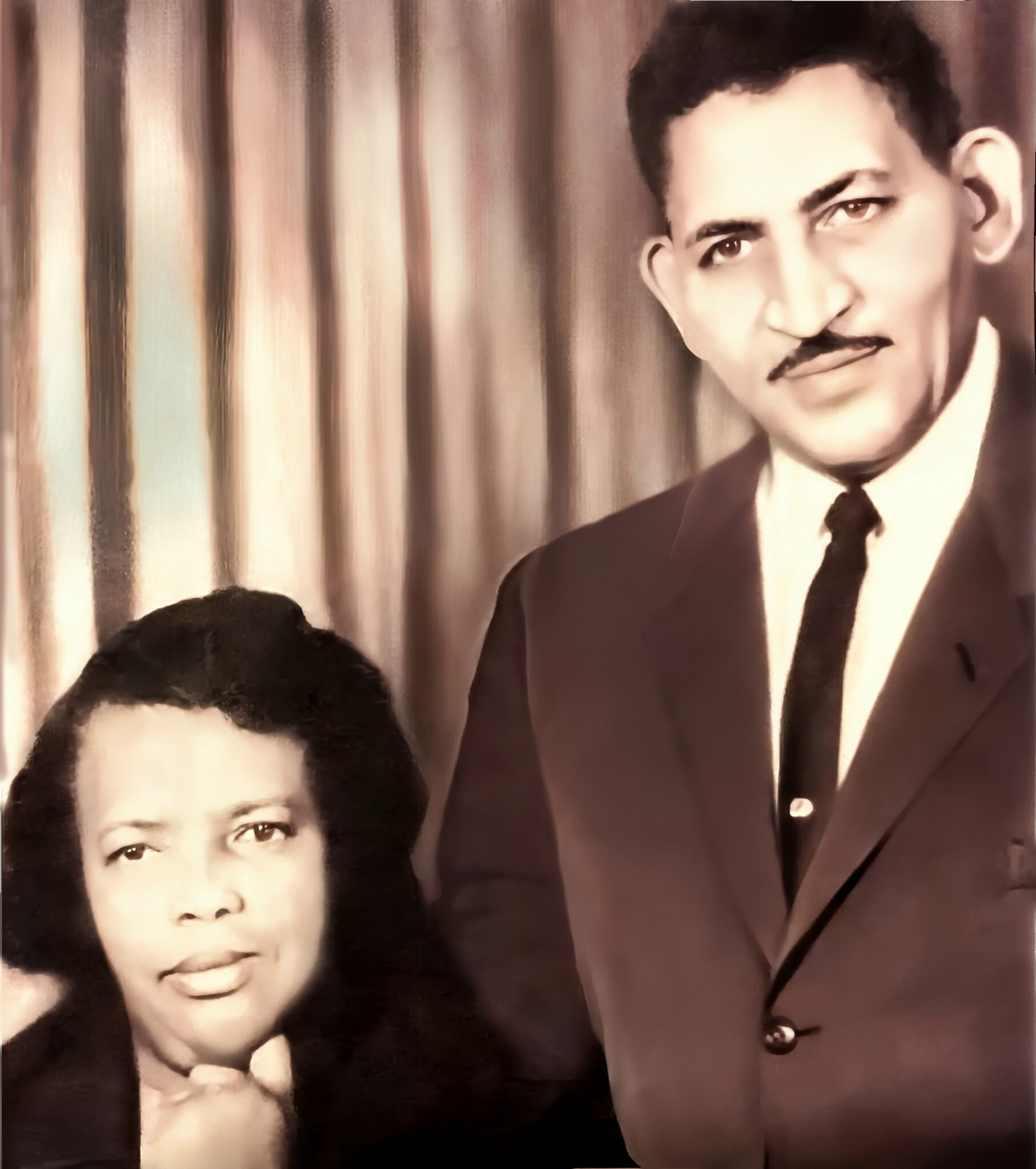 Vintage sepia portrait of two men in formal attire; man on the right wears a suit and tie with a mustache, the other man is partially visible on the left.