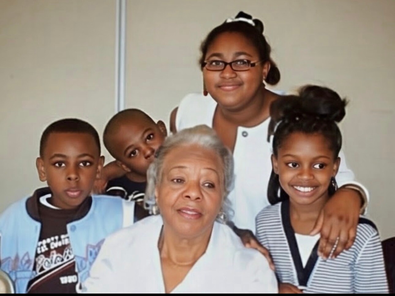 Grandmother seated center with two boys and two girls gathered around her for a warm family photo, everyone smiling.