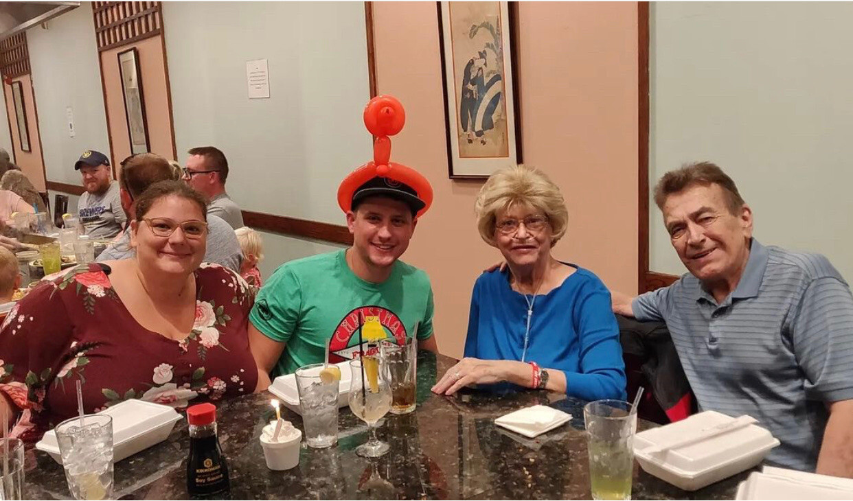 Four adults sit at a restaurant table, smiling for the photo, with drinks and takeout containers in front.