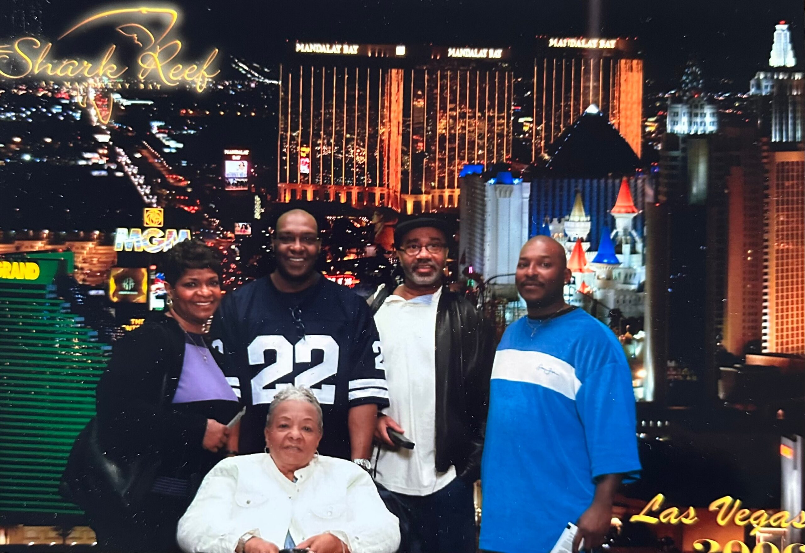 Group of five adults posing for a photo in front of a Las Vegas skyline backdrop, with casino signs visible in the background (MGM Grand).