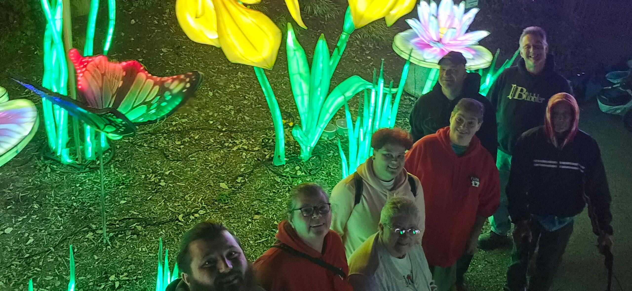 Group of people posing together at night in front of glowing neon garden sculptures.