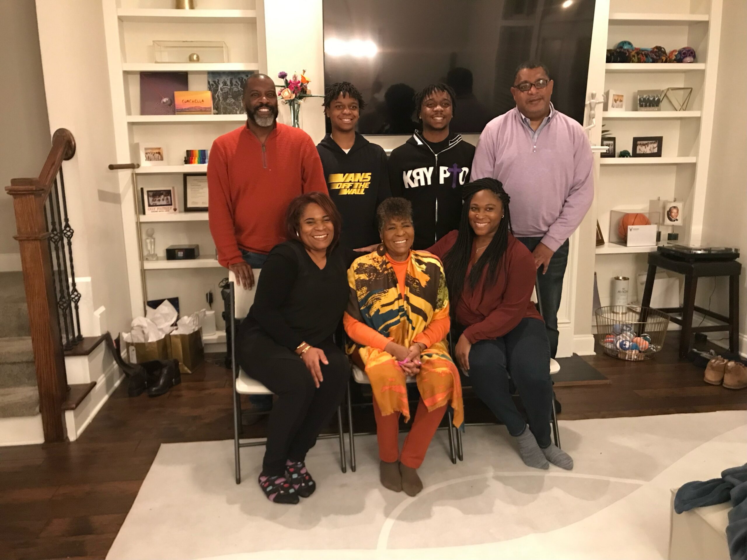 Group of seven people posing indoors in a living room, all smiling for the photo.