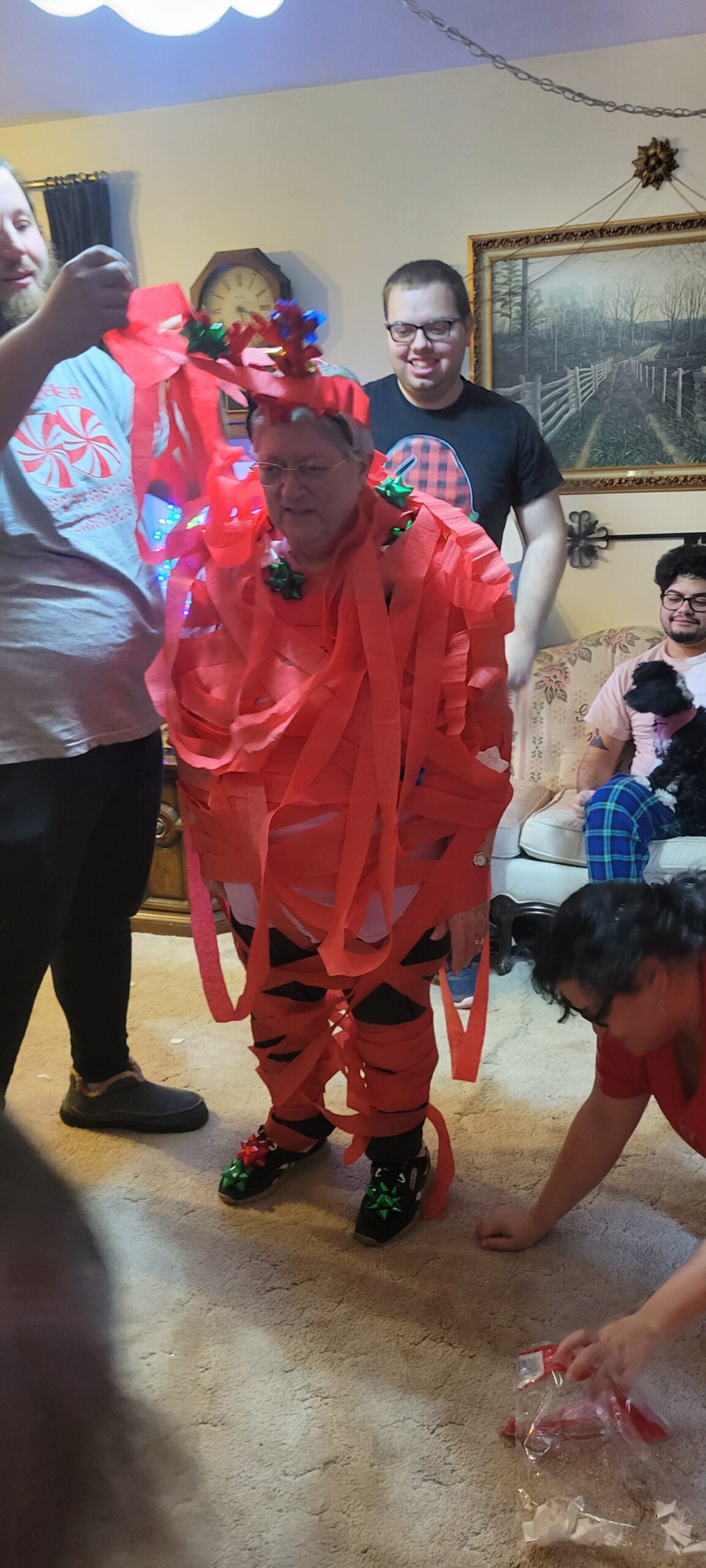 Person wearing a costume made of red streamers at a party, with others watching indoors.
