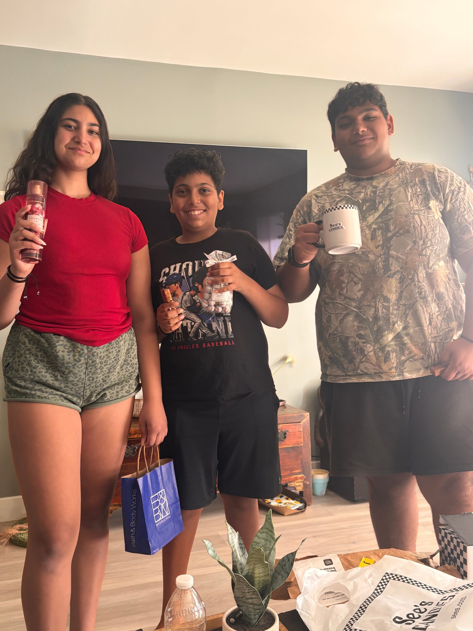Three people stand indoors, smiling at the camera, each holding a drink or snack.