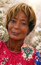 Portrait of an older woman with short light brown hair, wearing a red embroidered blouse, smiling softly.