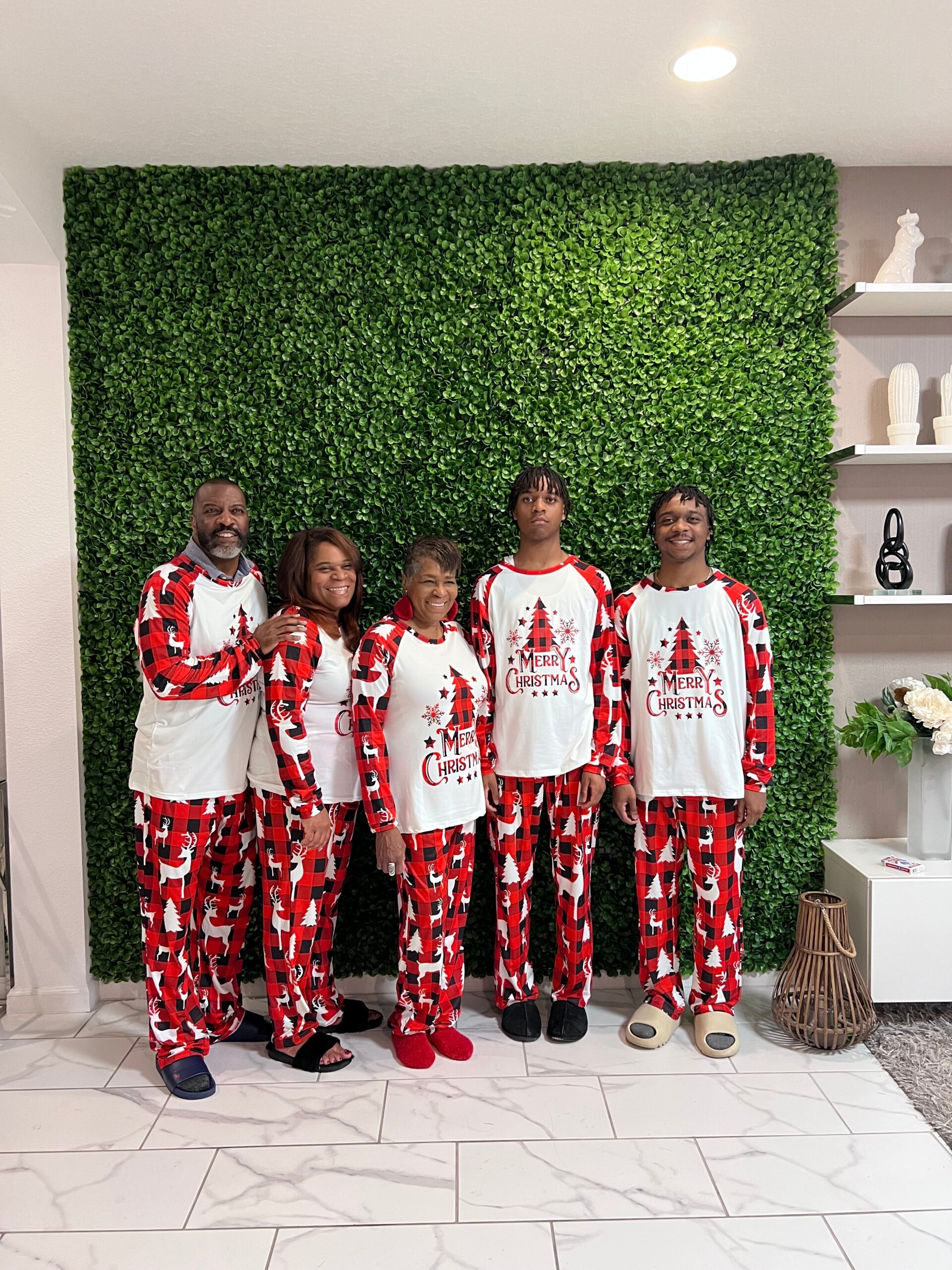 Five people in matching red-and-white Christmas pajamas posing in front of a green leafy wall, festive 
