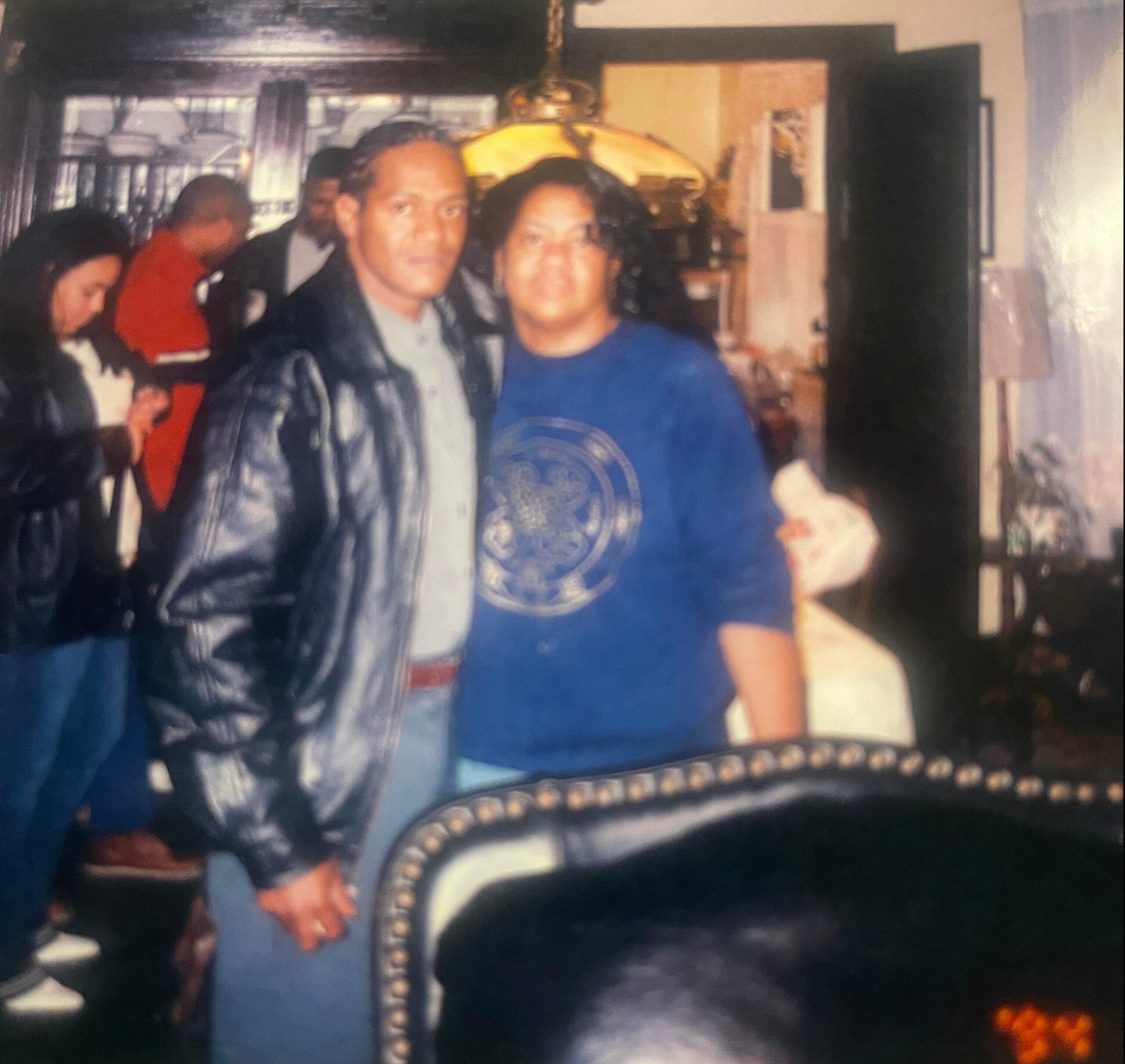 Blurry indoor photo of a man and a woman standing close together in a living room, with a lamp and decorative furniture in the background.