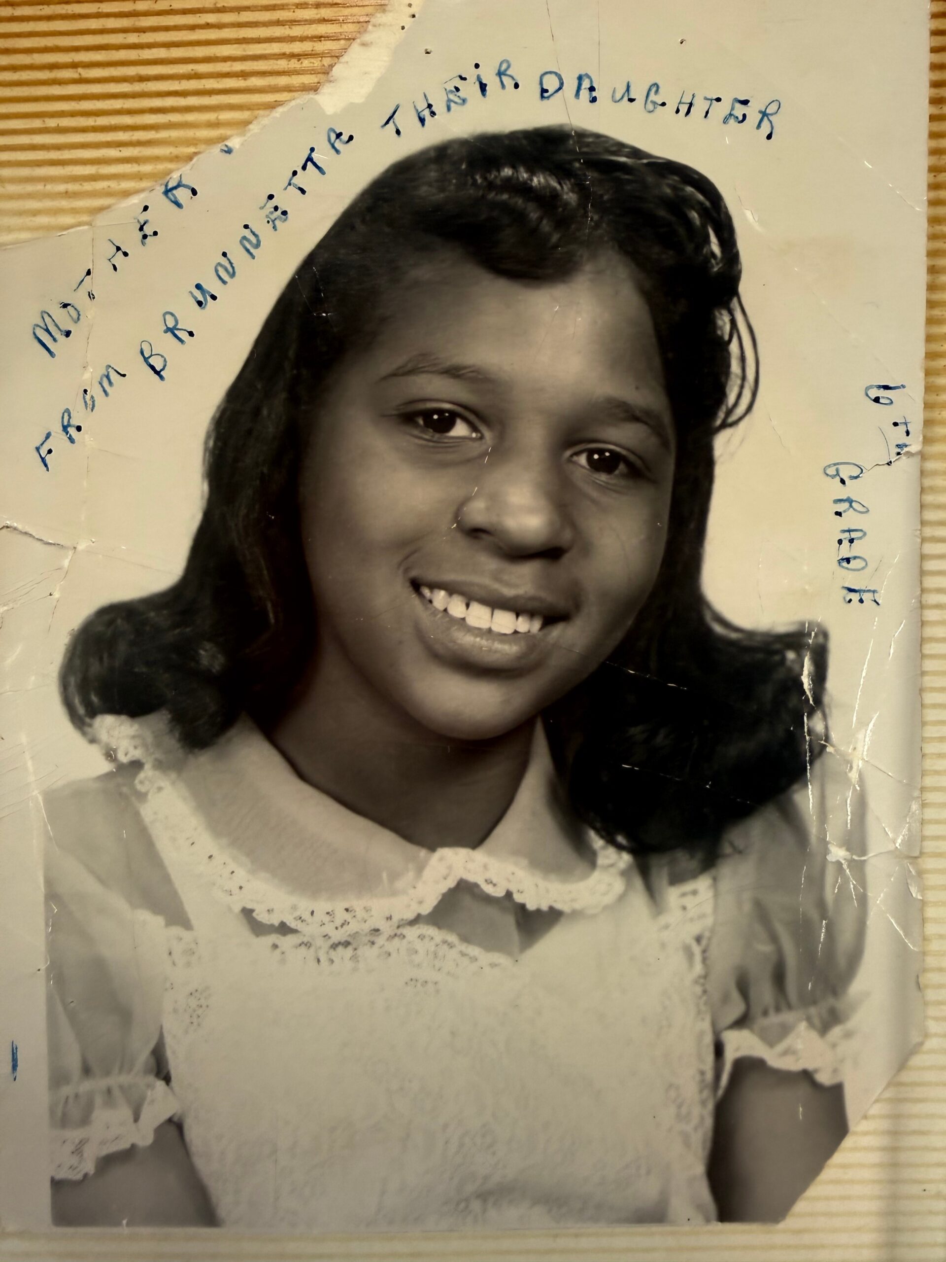 Vintage black-and-white portrait of a smiling girl with dark hair, wearing a lace-collared blouse; handwritten text arches above her head.