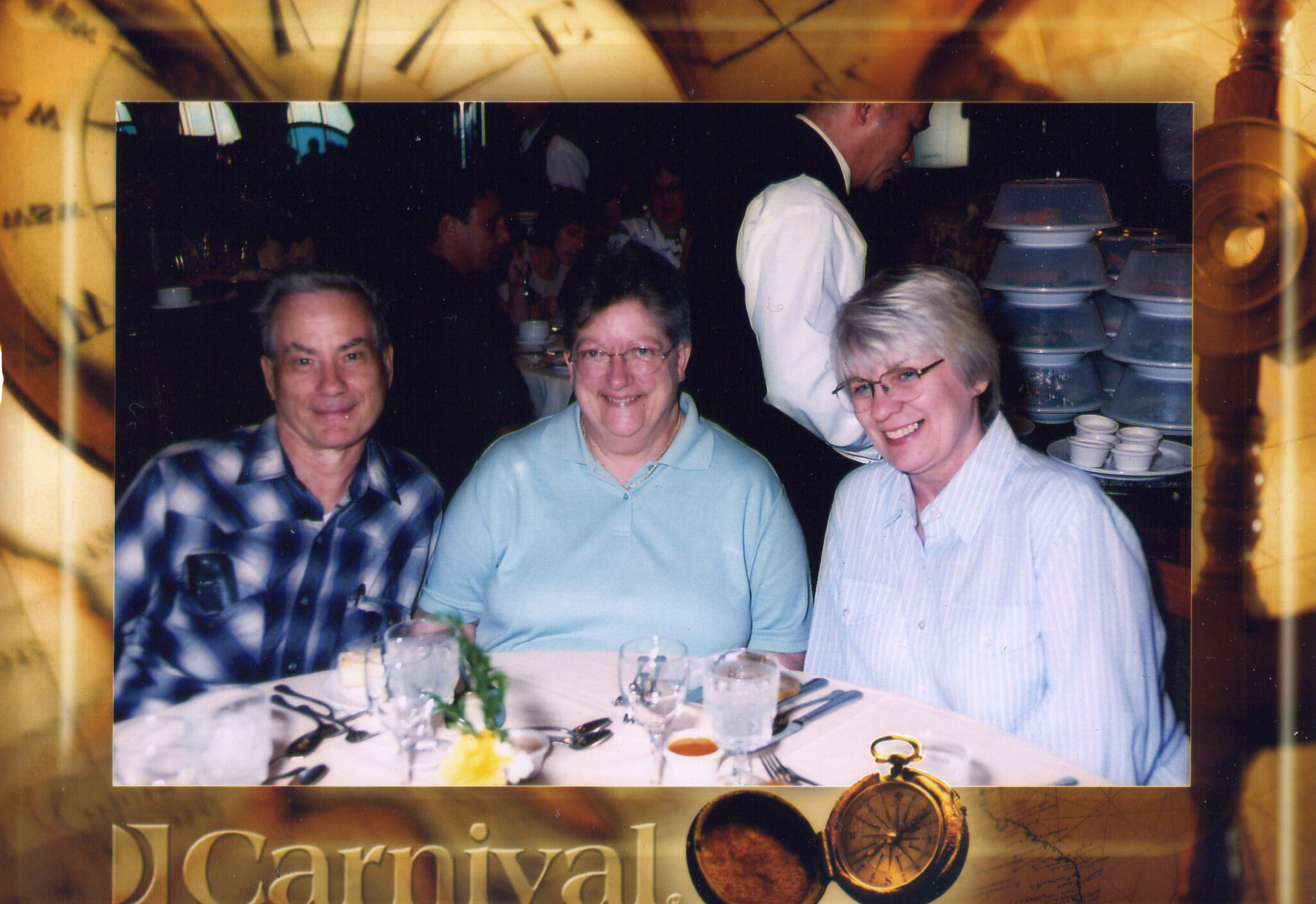 Three smiling adults seated at a banquet table with plates, drinks, and a small bouquet in the foreground.