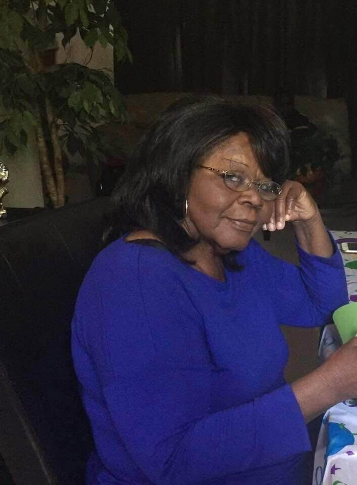 Smiling woman with glasses in a royal blue top resting her chin on her hand at a table.