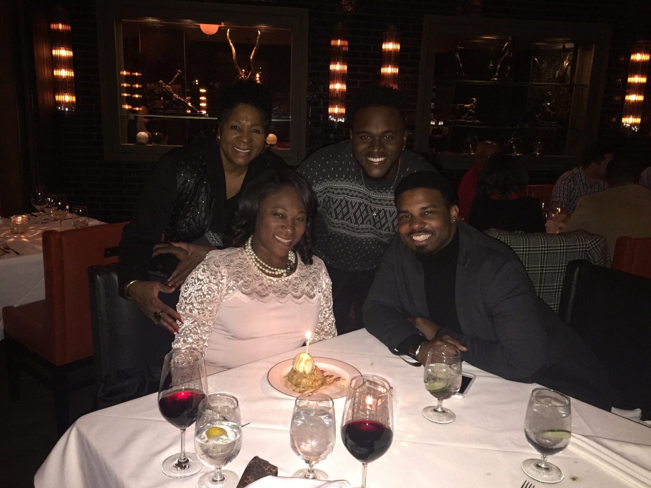 Four friends at a candlelit restaurant posing for the photo with a plated dessert and drinks on the table in front of them.