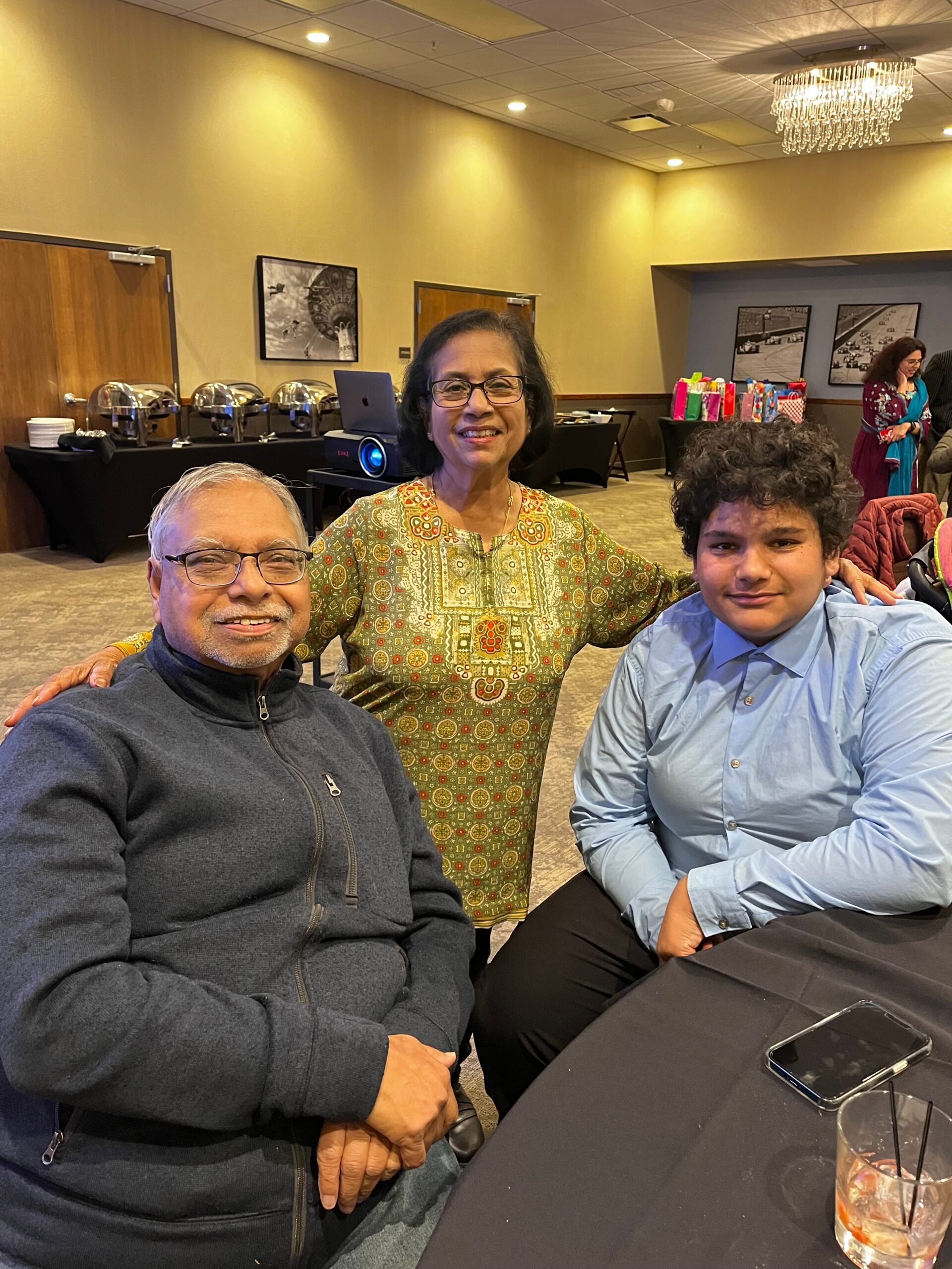 Three people smile for a photo at a banquet table in a conference hall, with buffet chafing dishes in the background.