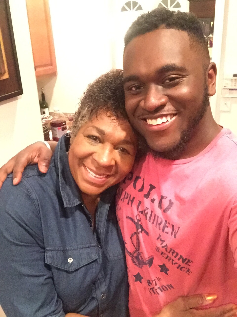 Smiling young man and older woman hug in a kitchen.