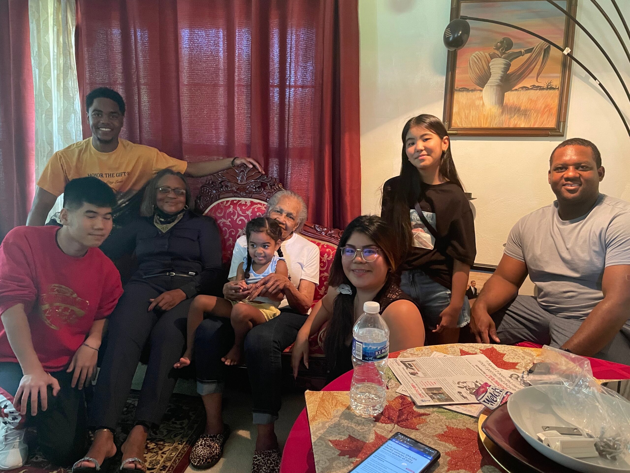 Group of family and friends posing for a photo on a red-upholstered couch in a living room, smiling at the camera.