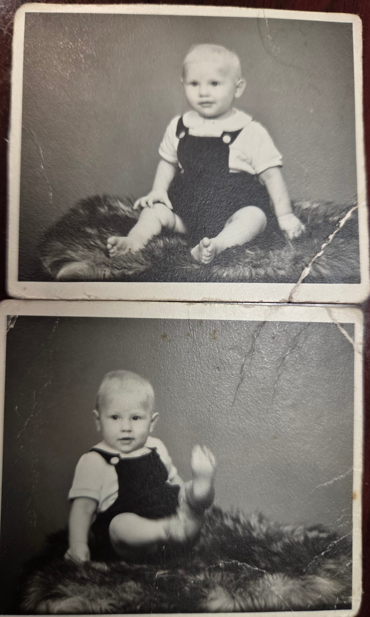 Baby sitting on a fluffy rug in light shirt and dark overalls, looking at the camera.