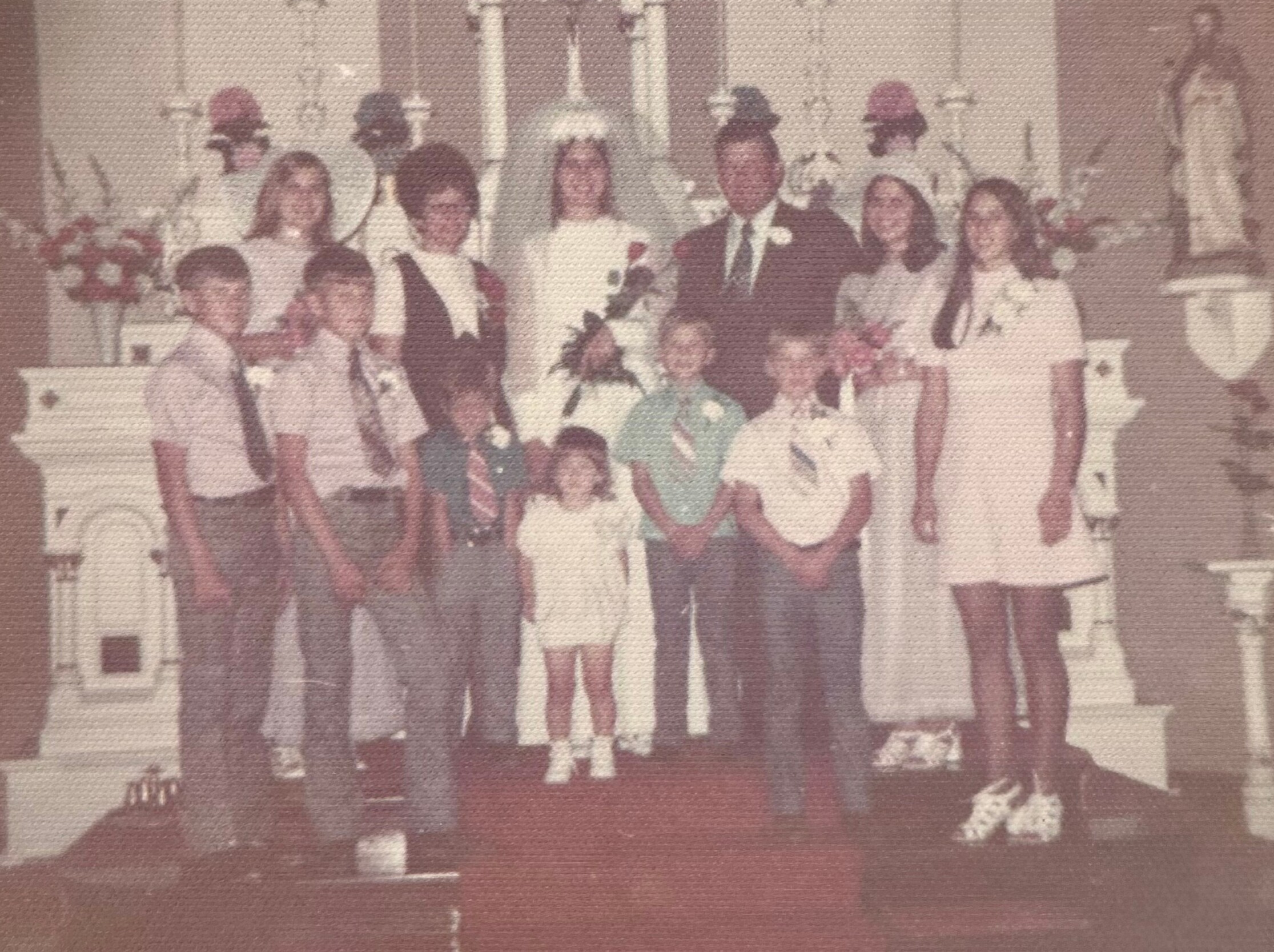 Group of people in a church-like setting posing for a formal photo, some in white robes and others in dark outfits, with flowers nearby.